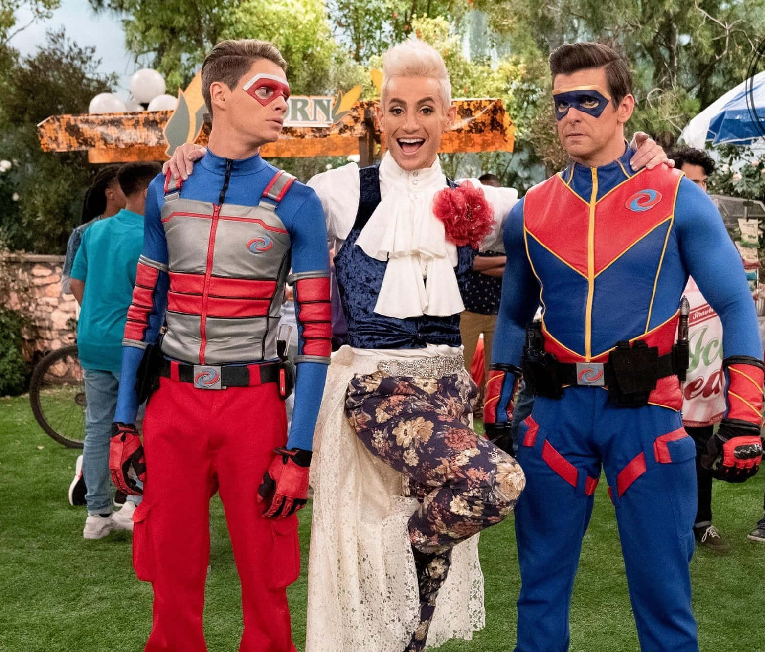 nickelodeon 桌布 壁紙 — 三位身穿鮮豔超級英雄服裝的裝扮英雄，在草地上愉快地擺姿勢，背景有樹木和一個質樸的標誌。