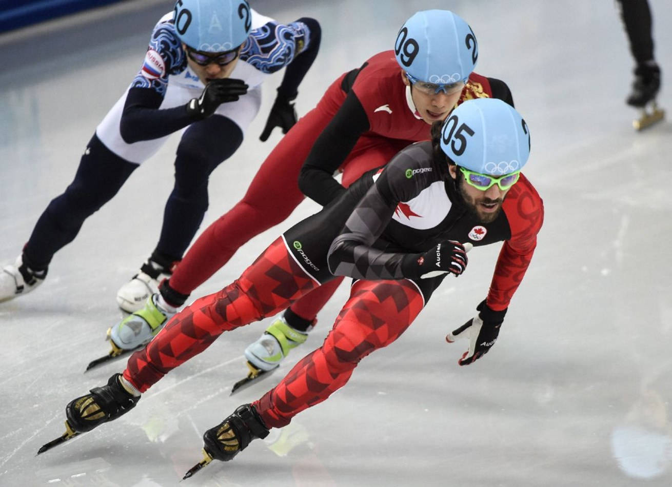 Olympics 桌布 壁紙 — 三位速度滑冰選手在激烈競爭中，在室內冰場的彎道上傾身轉彎，進行一場高風險的比賽。
