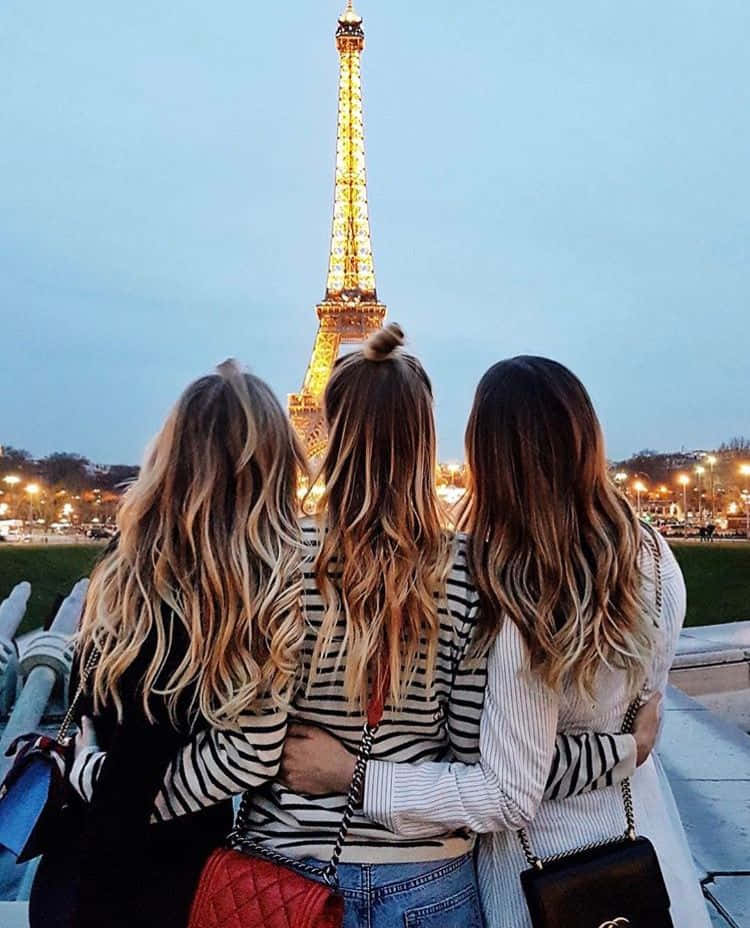 Three Friends 桌布 壁紙 — 三位長髮朋友在黃昏時分擁抱，凝視著閃閃發光的艾菲爾鐵塔。