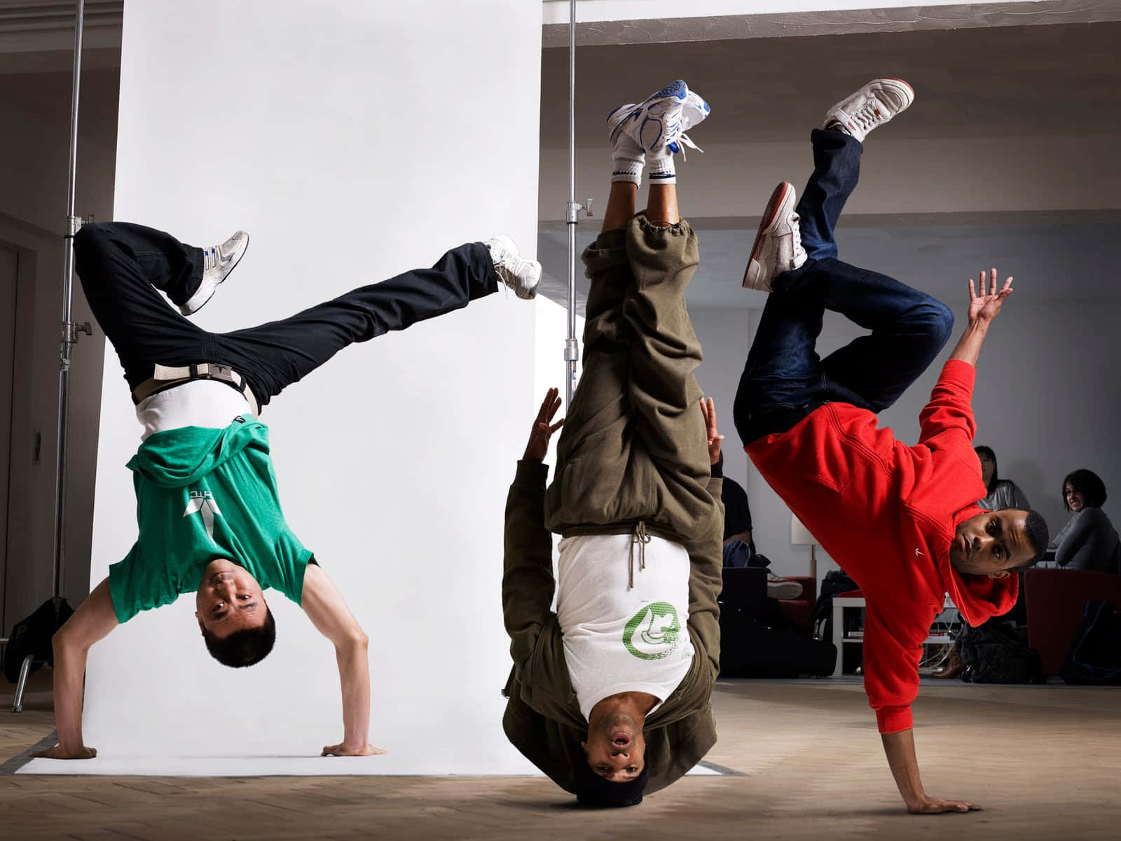 hiphop 桌布 壁紙 — 三位霹靂舞者在白色背景和木地板的錄影室中表演動態倒立。