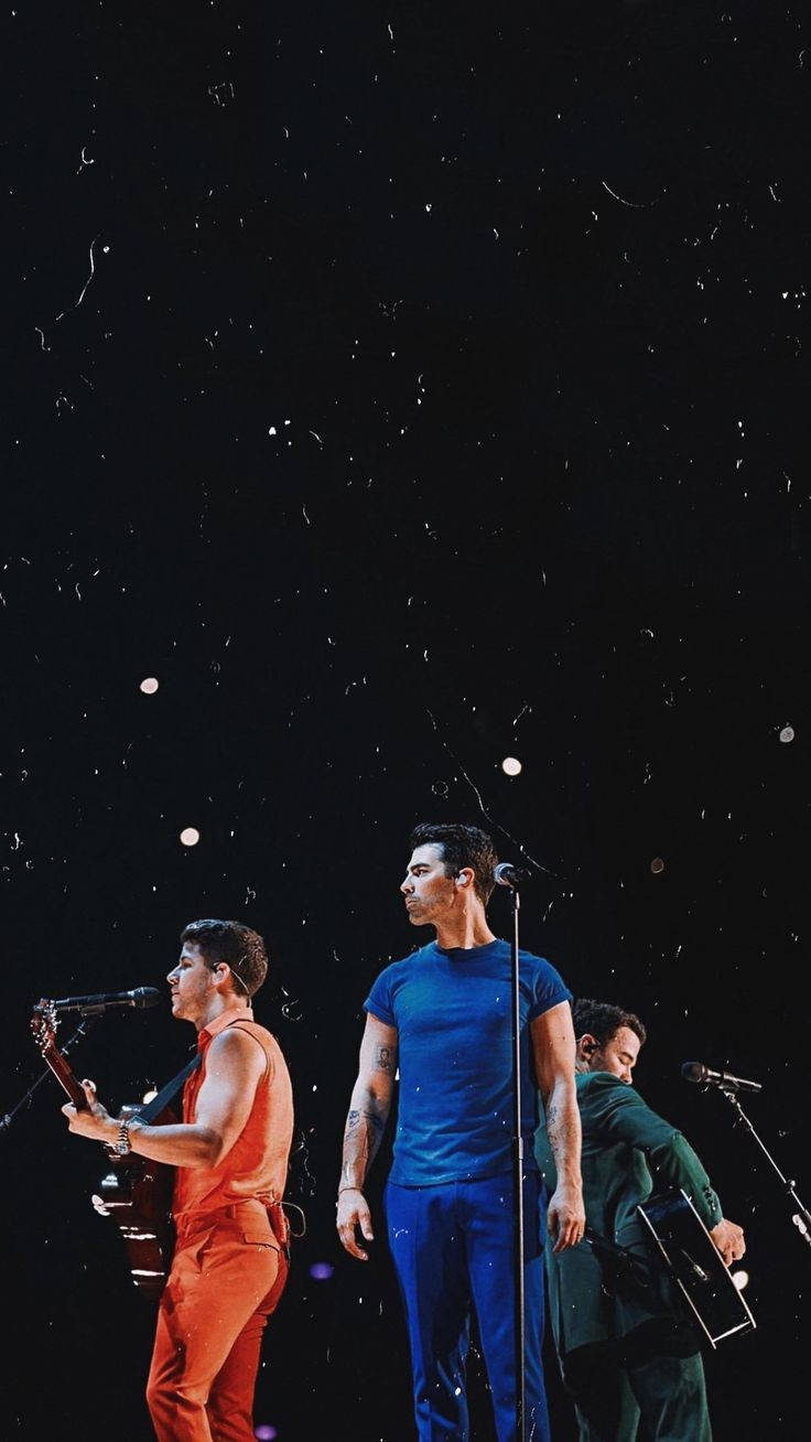 Jonas Brothers 桌布 壁紙 — 三位音樂家在星光燈光下表演，周圍有五彩紙屑飄落。
