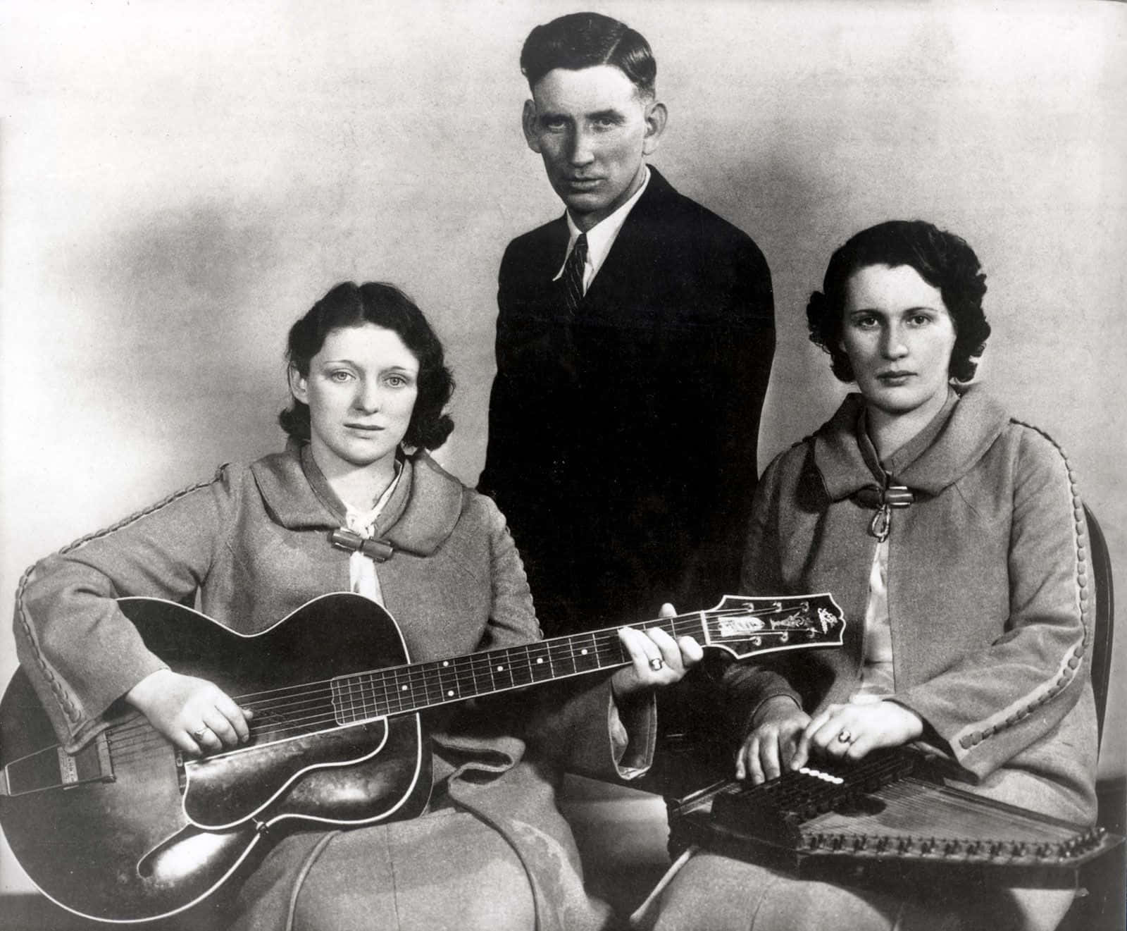 Carter Family 桌布 壁紙 — 三位音樂家在素色背景前拿著吉他和豎琴擺姿勢的復古黑白工作室肖像。