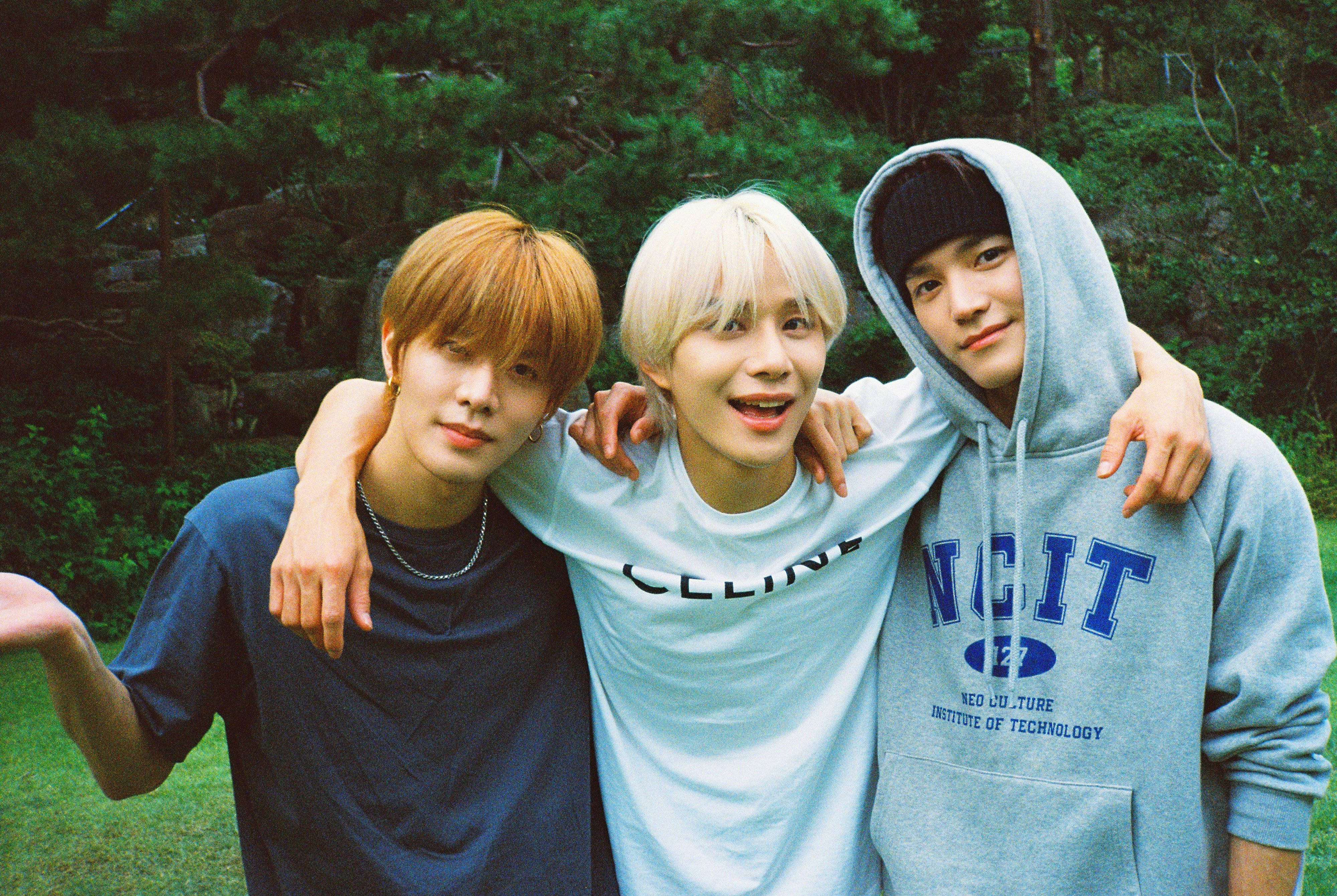 Nct 桌布 壁紙 — 三位頭髮色彩繽紛的年輕男子在森林中愉快地擺姿勢，互相搭著肩膀。