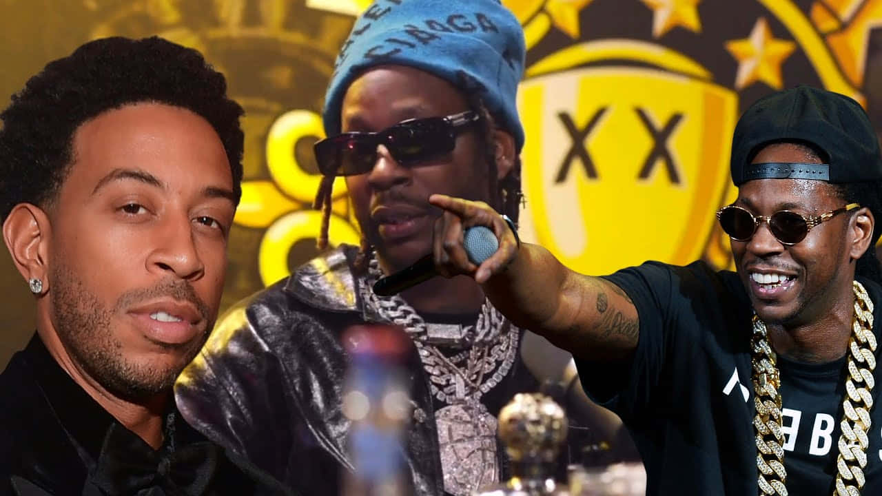 2 Chainz 桌布 壁紙 — 三位饒舌歌手在一個豪華活動中自信地擺姿勢，背景有金色獎盃和品牌標誌。