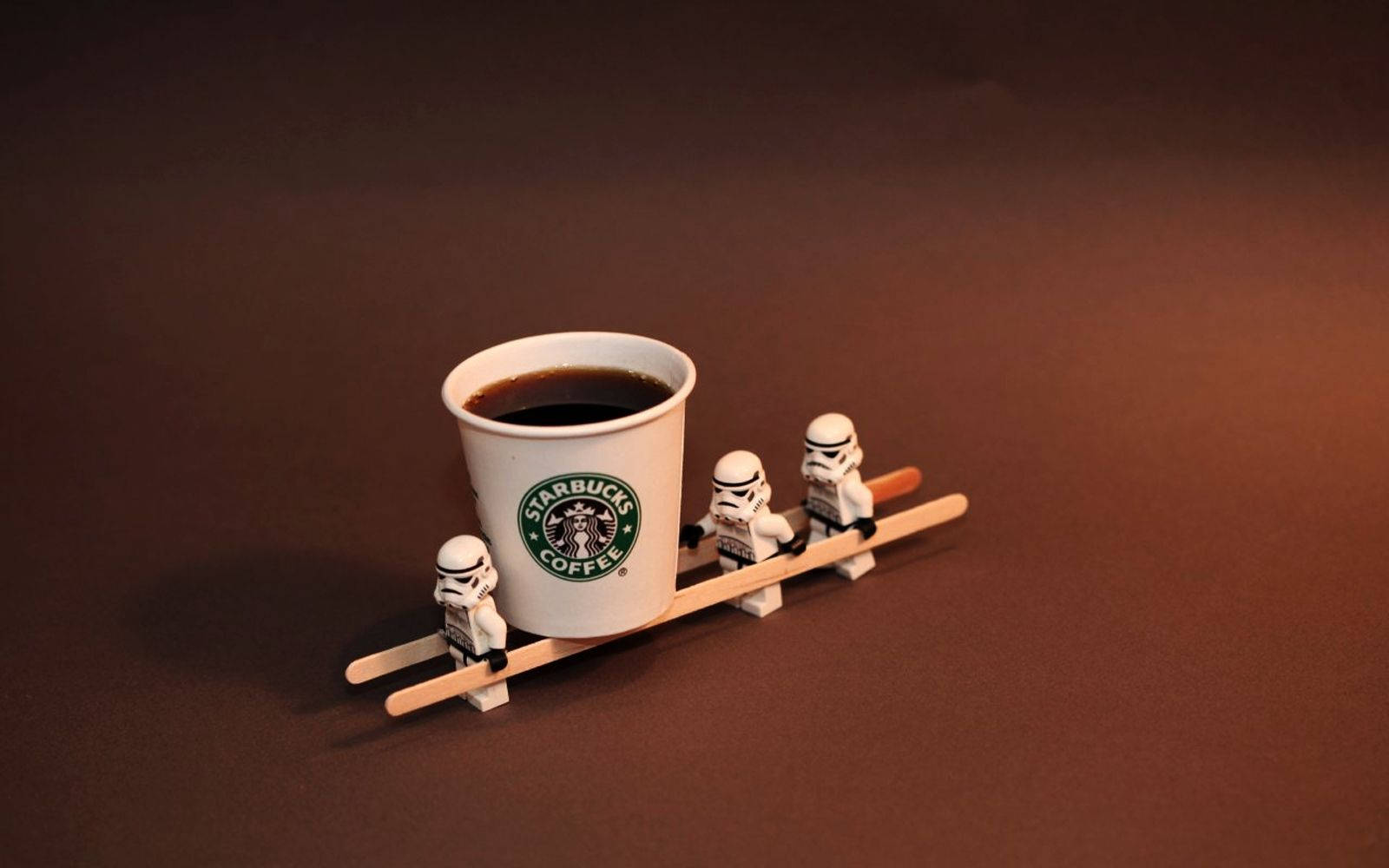 三個 LEGO 白兵用木製雪橇拉著一杯 Starbucks 咖啡杯。