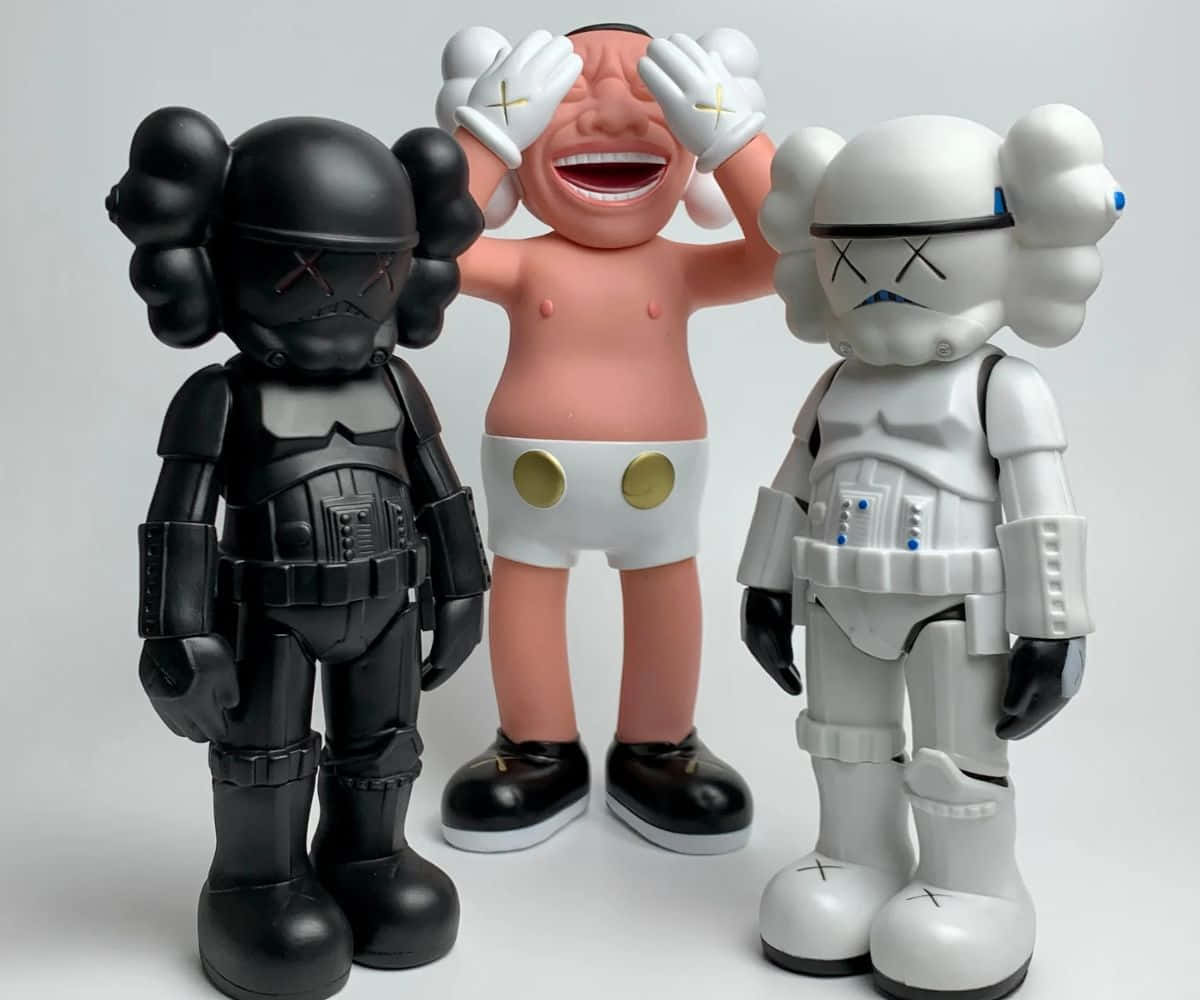 Kaws Stormtrooper 桌布 壁紙 — 三個KAWS收藏級人偶並排站立：一個黑色風暴兵、一個白色風暴兵和一個穿著白色尿布的笑臉嬰兒。