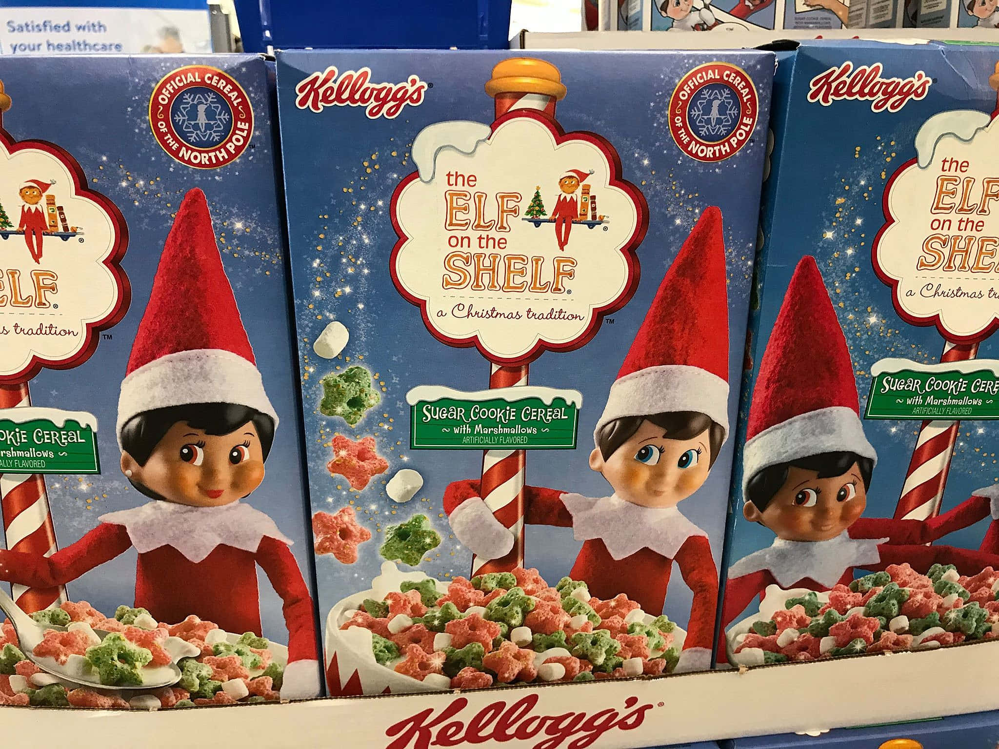 聖誕節 桌布 壁紙 — 三個Kellogg's Elf on the Shelf穀物盒展示戴紅帽的快樂精靈，在雪白的北極背景下拿著星形穀物和棉花糖。