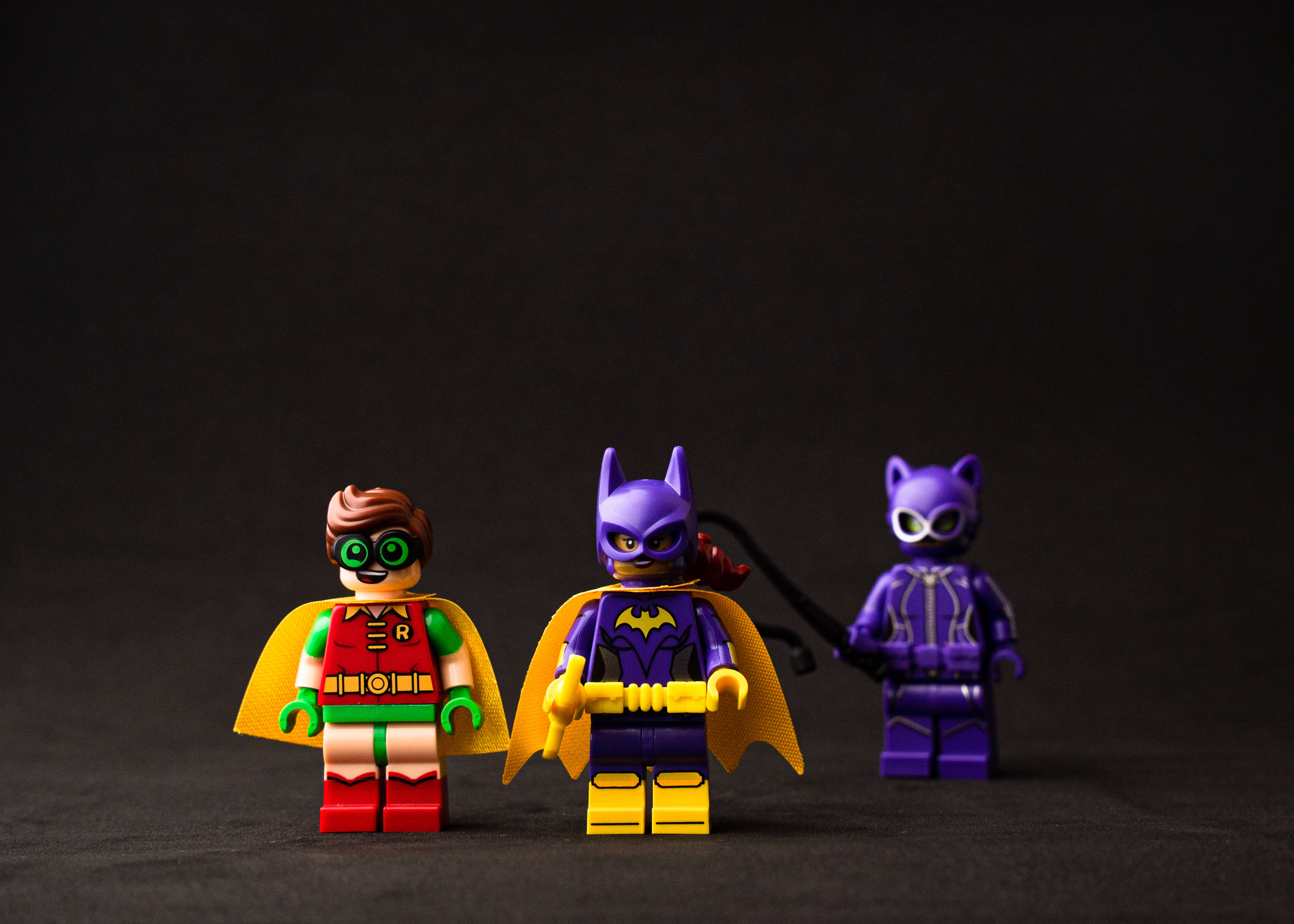 Catwoman 桌布 壁紙 — 三個LEGO超級英雄人偶羅賓、蝙蝠女和貓女站成一排，背景為深色。