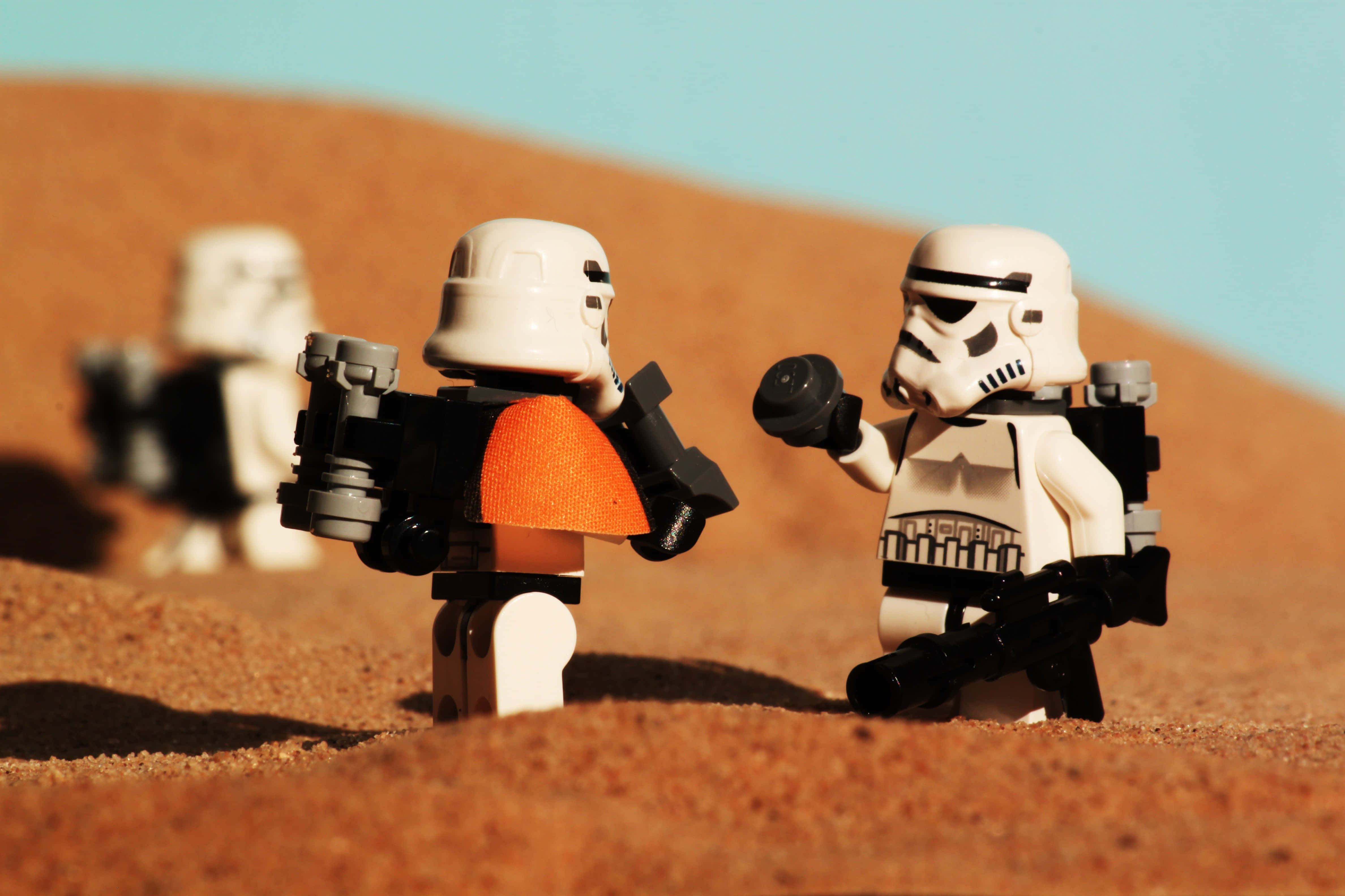 Tatooine 桌布 壁紙 — 三個LEGO風暴兵站在沙漠中，一個手持爆能槍，另一個穿著橙色背心。