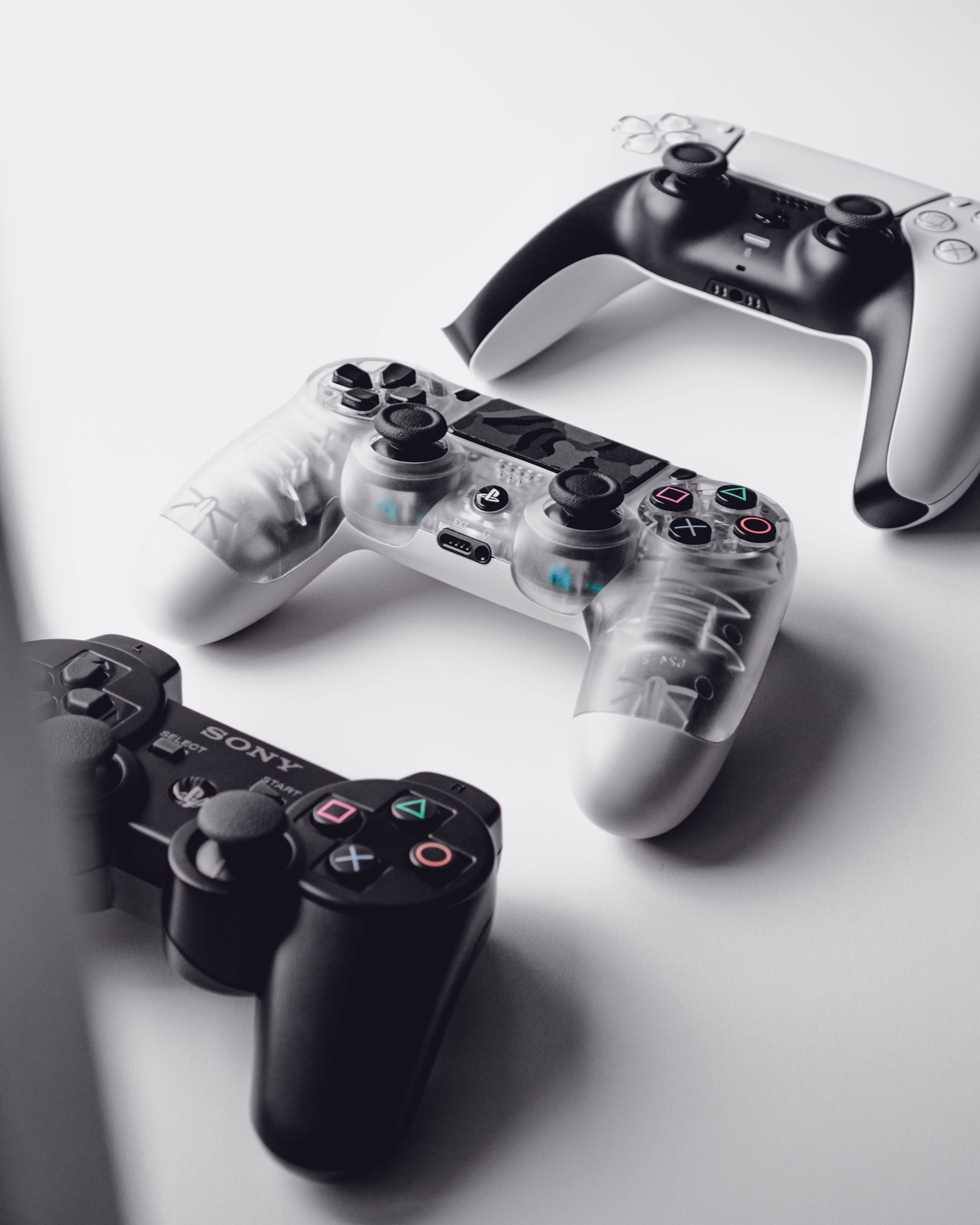 PS3 桌布 壁紙 — 三個Sony PlayStation控制器，採用黑色半透明和白色設計，排列在簡約的白色表面上。