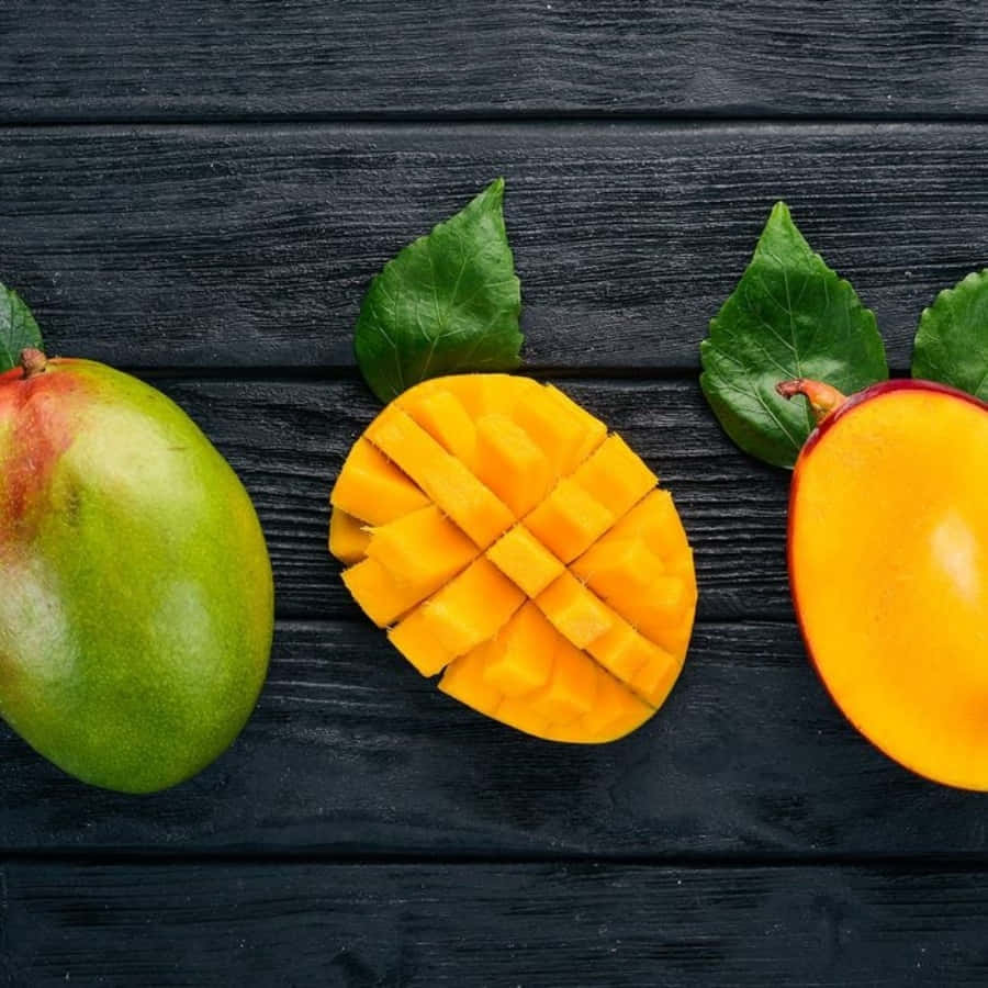 Mango 桌布 壁紙 — 三個不同狀態的芒果——一個完整綠色、一個切丁、一個對半切——放在深色木板上，搭配新鮮樹葉。