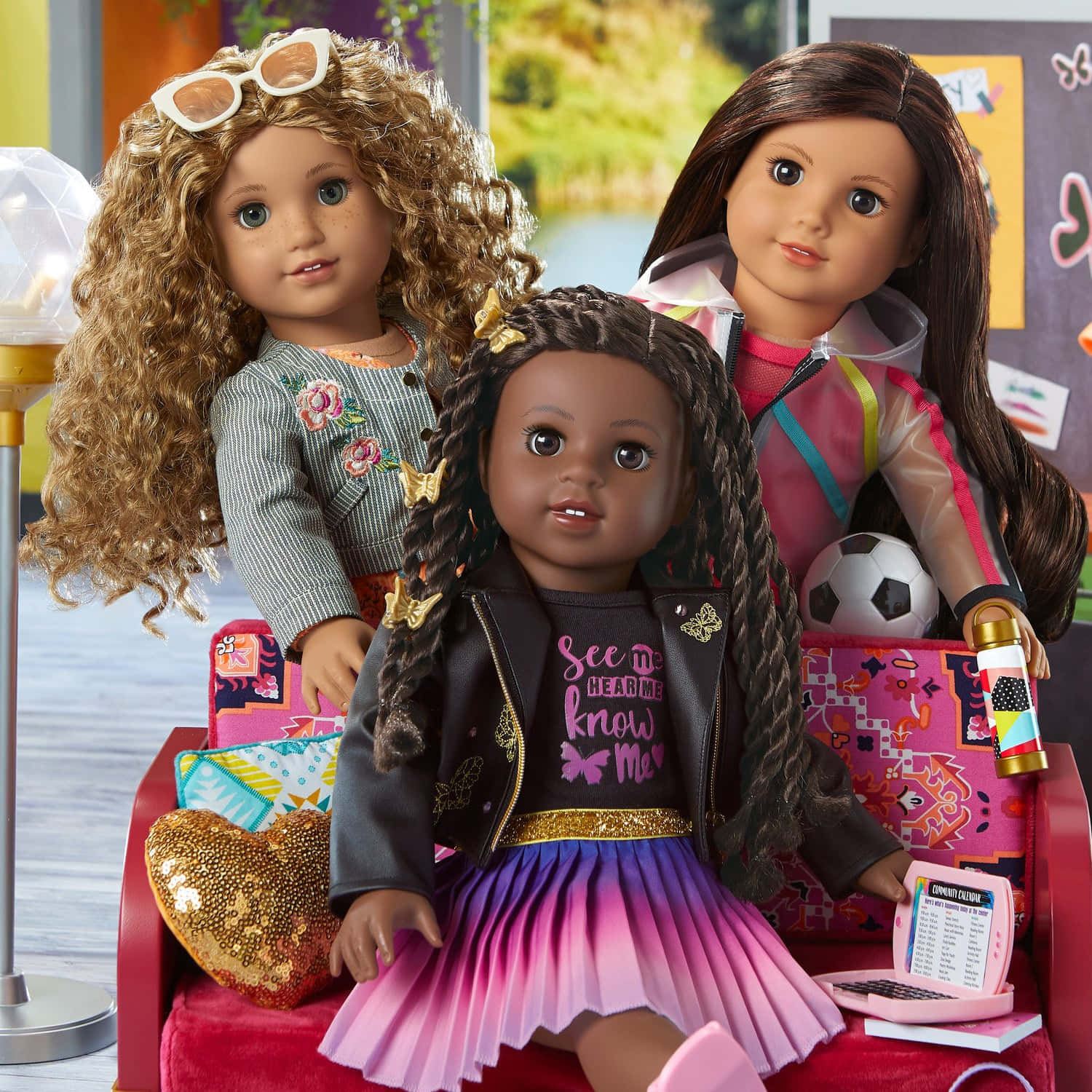 american girl 桌布 壁紙 — 三個不同的娃娃，穿著色彩繽紛的服裝和配件，一起坐在紅色沙發上，在一個充滿活力和玩樂氛圍的房間裡。