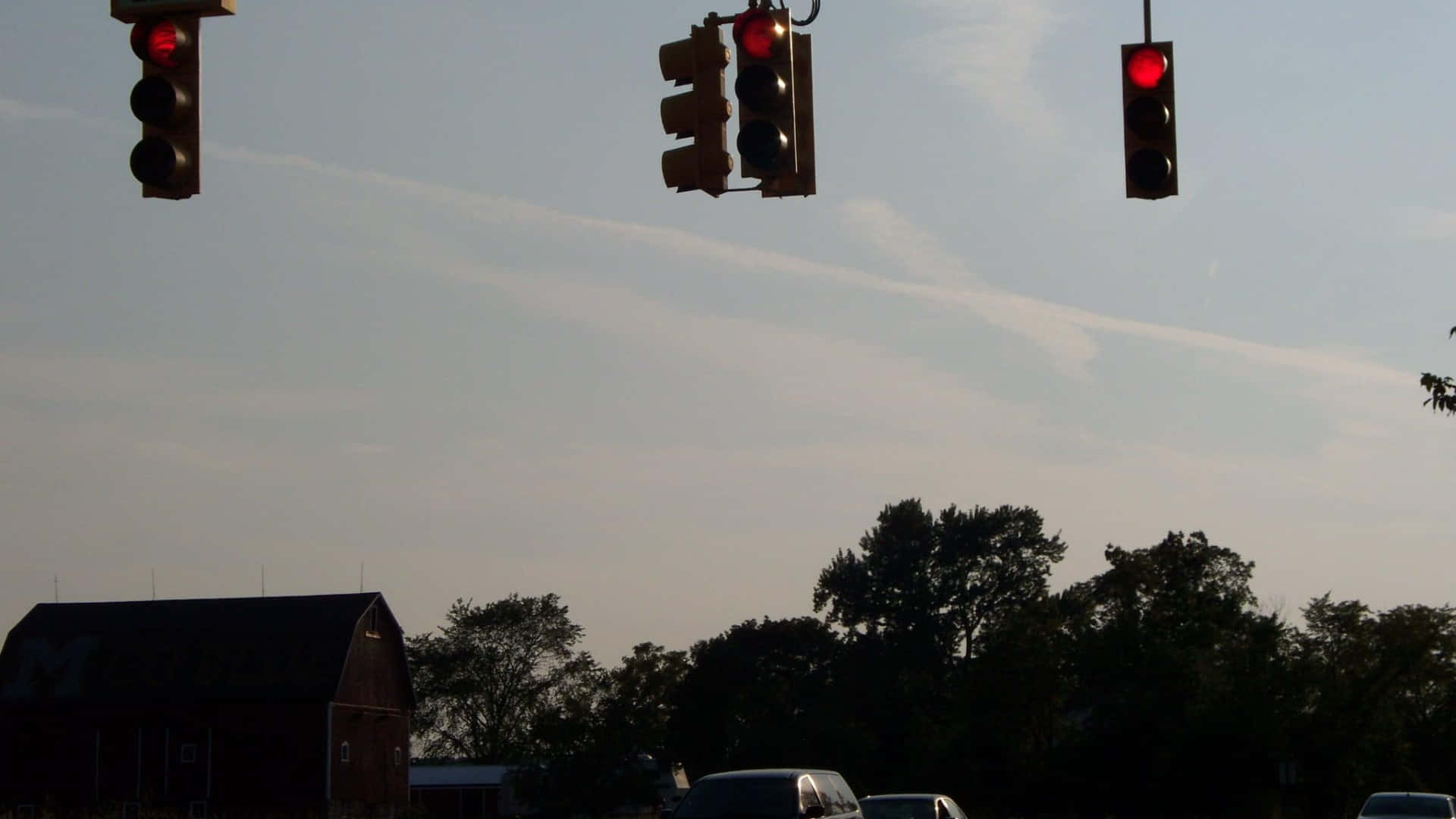 Stop Light 桌布 壁紙 — 三個交通燈在黃昏時分，於蒼白的天空襯托下，在剪影般的樹木和穀倉上方發出紅光。