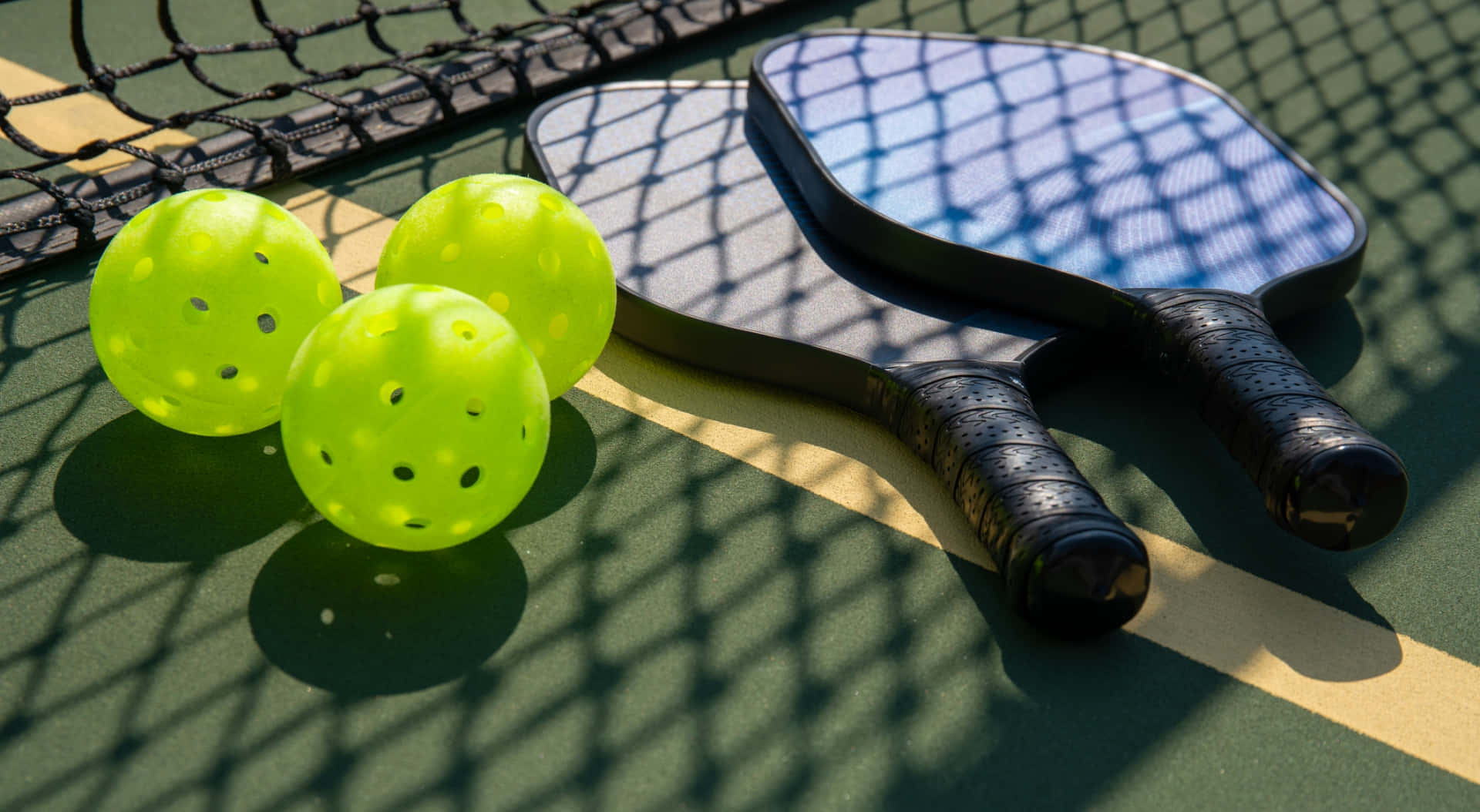 Pickleball 桌布 壁紙 — 三個亮綠色匹克球和兩個球拍放在綠色球場上，球網投下清晰的陰影。
