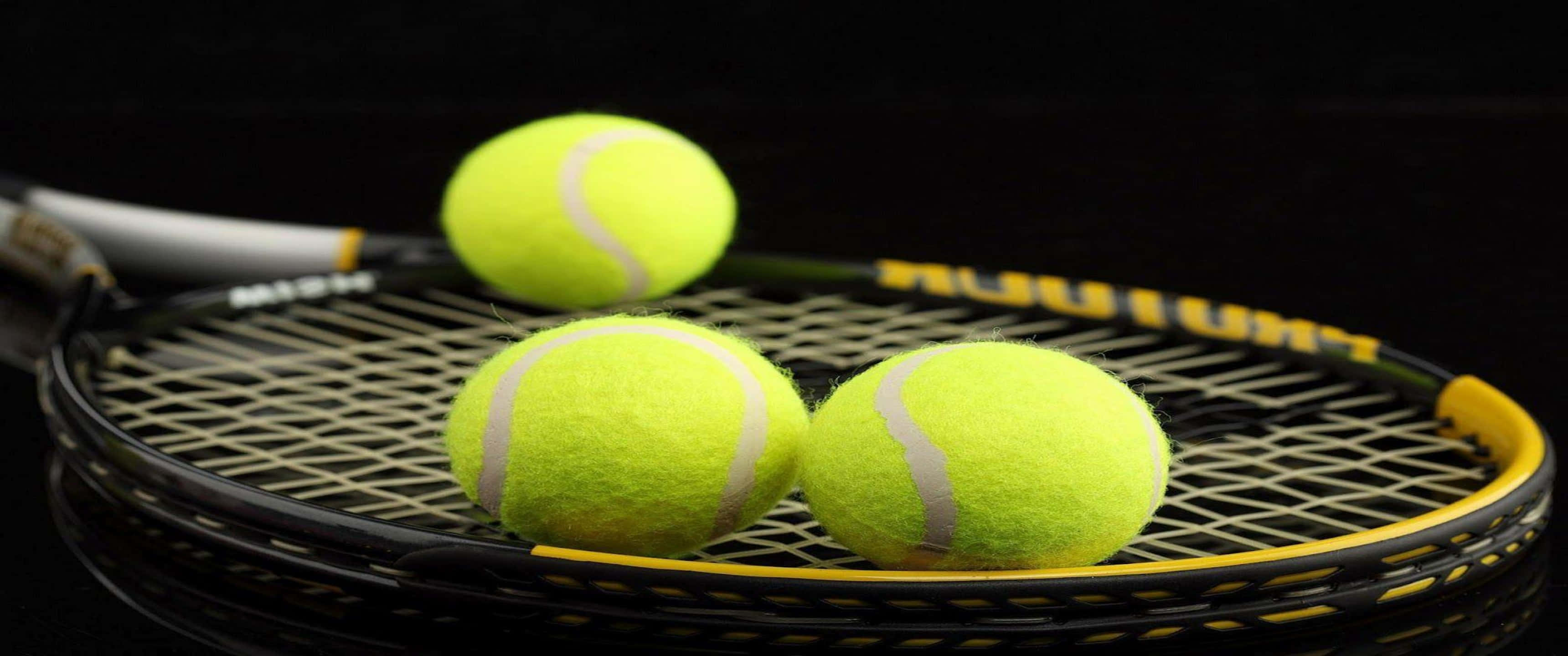 3440x1440p Tennis 桌布 壁紙 — 三個亮黃色網球放在一個黑色和黃色的球拍上，背景為深色。
