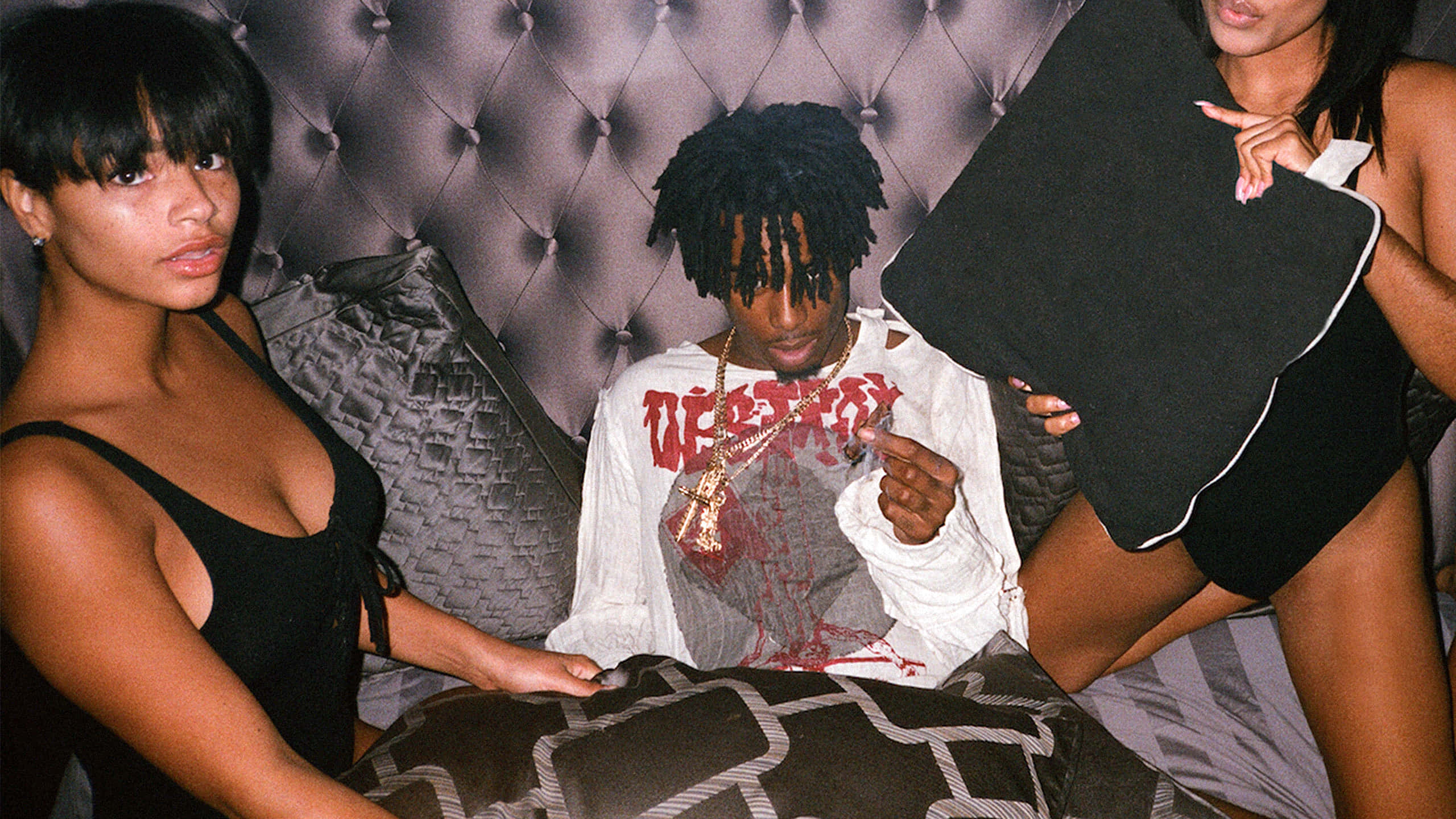 playboi carti pfp 桌布 壁紙 — 三個人在昏暗的豪華房間裡，在一張有搶眼圖案和金鏈的簇絨床上休息。