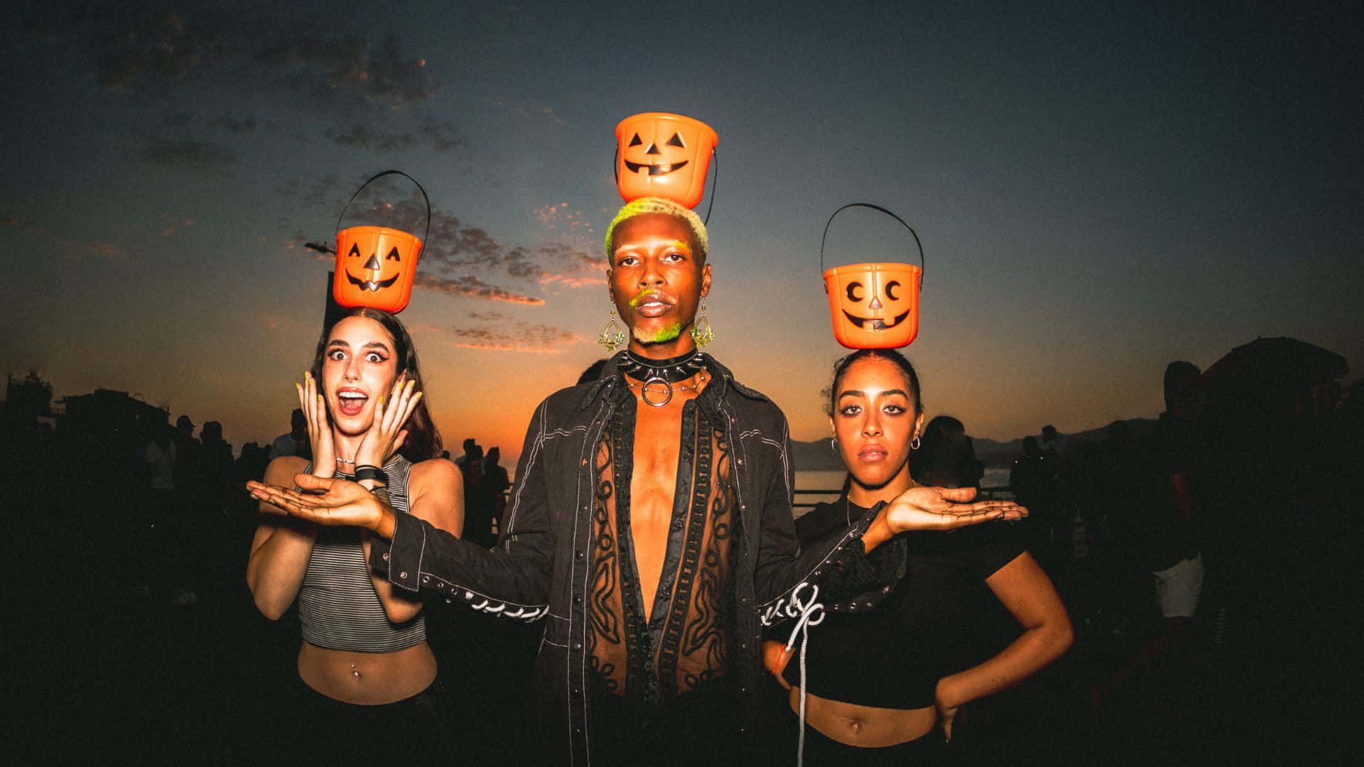 Halloween Costumes 桌布 壁紙 — 三個人在暮色天空下，將南瓜燈籠桶平衡在頭上擺姿勢。