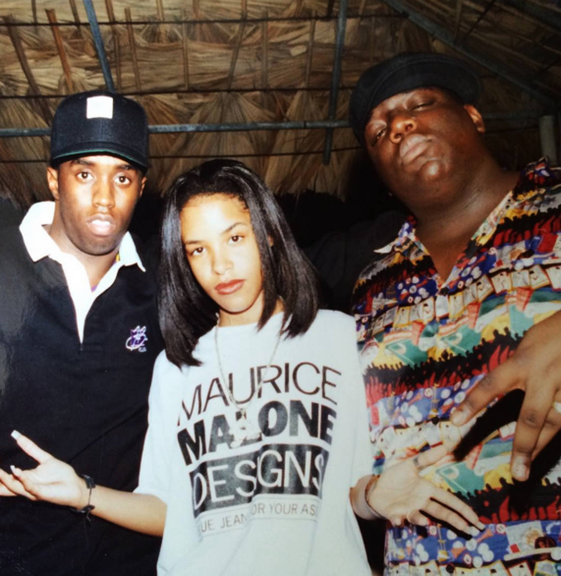 90s Rapper 桌布 壁紙 — 三個人在茅草屋頂下自信地擺姿勢，穿著大膽圖案和休閒街頭服飾。