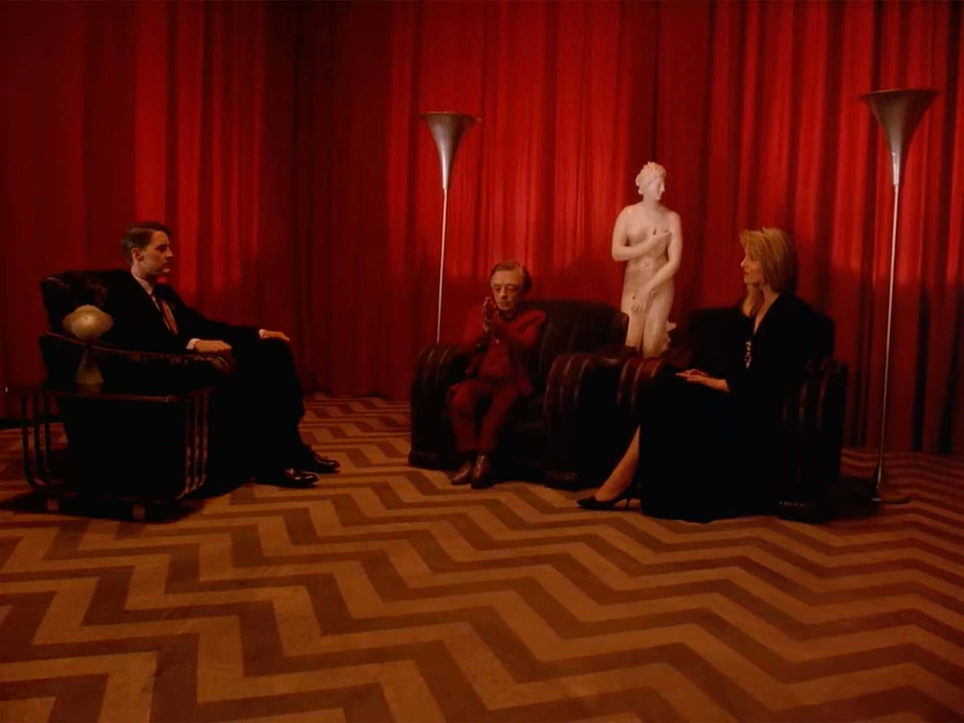 Red Room 桌布 壁紙 — 三個人坐在深色椅子上，背景是深紅色窗簾、白色雕像和人字形圖案地毯。