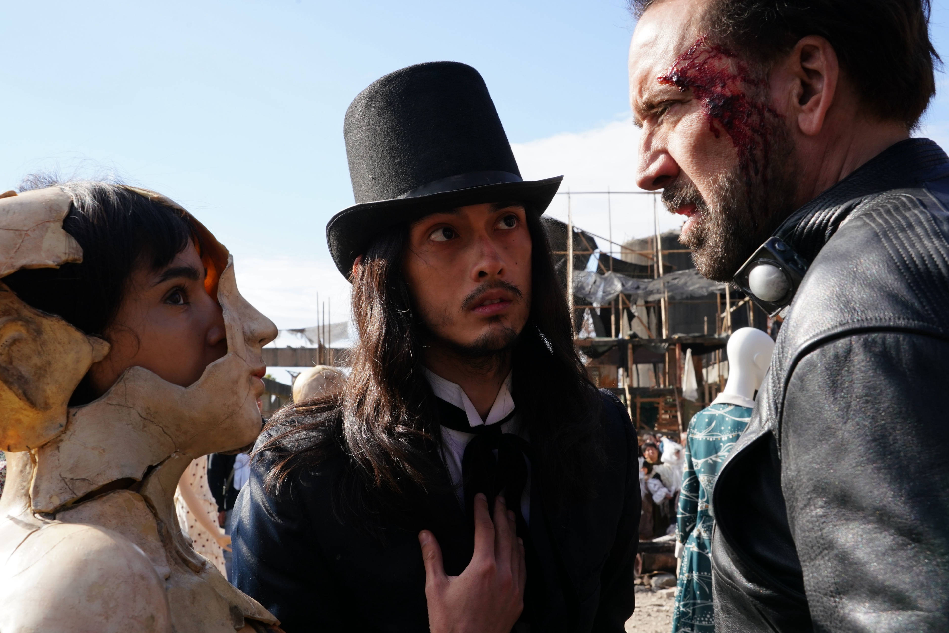 prisoners of the ghostland 桌布 壁紙 — 三個人物在陽光照耀的垃圾場對峙，一個戴著骷髏面具，另一個戴著高帽，第三個滿臉是血。