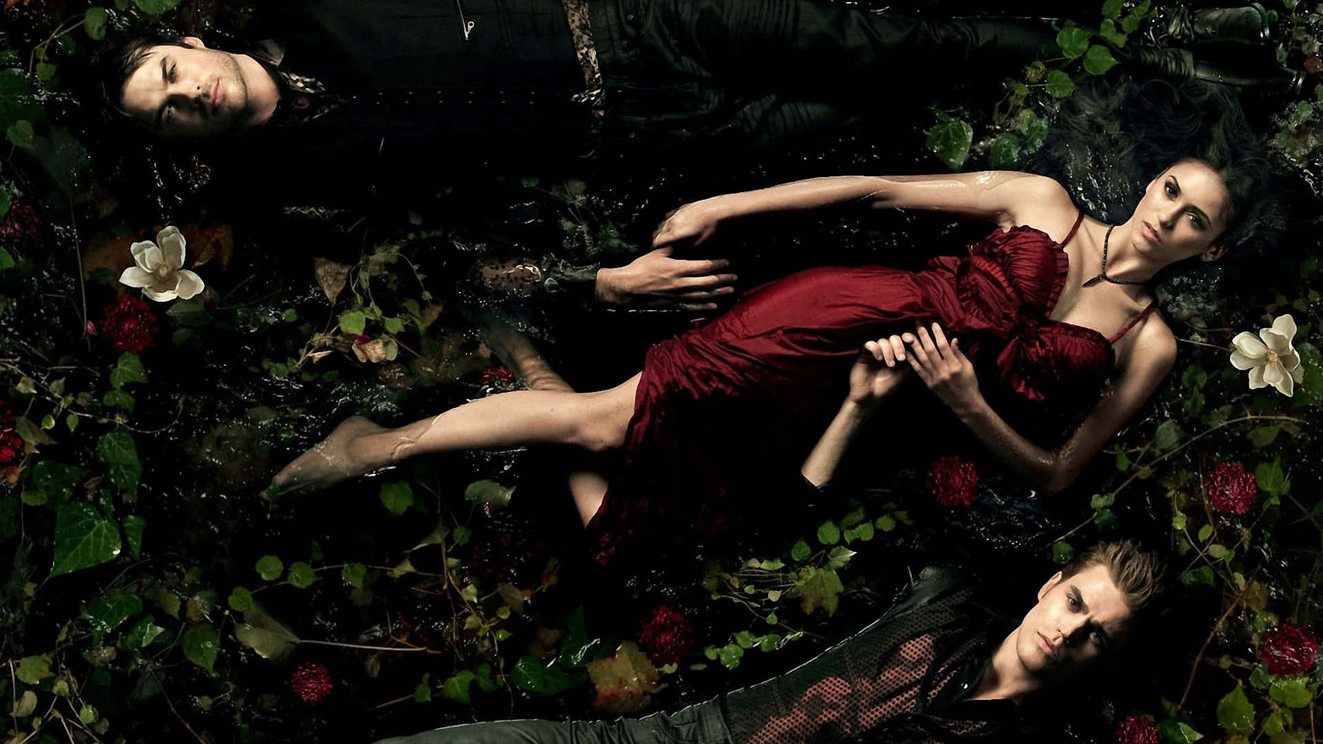 Vampire Diaries Desktop 桌布 壁紙 — 三個人物在黑暗的水中漂浮，周圍環繞著茂密的綠色植物和紅白花朵，在氛圍燈光下。