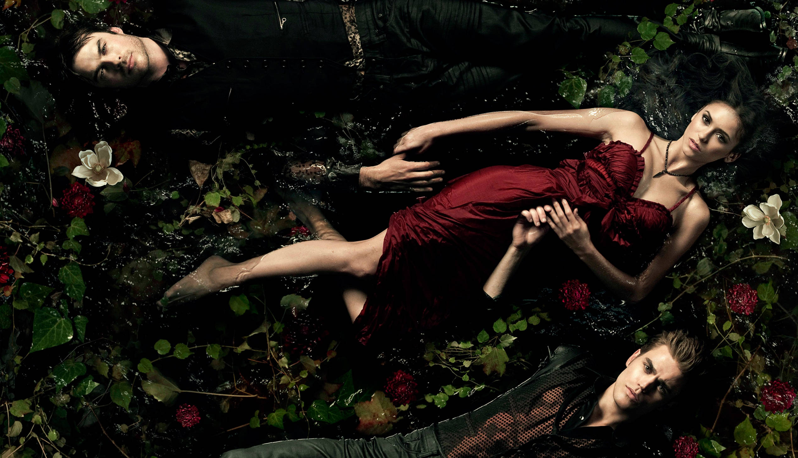 Vampire Diaries 桌布 壁紙 — 三個人物漂浮在黑暗的水中，周圍環繞著茂密的綠色植物和紅白花朵，在陰鬱的燈光下。
