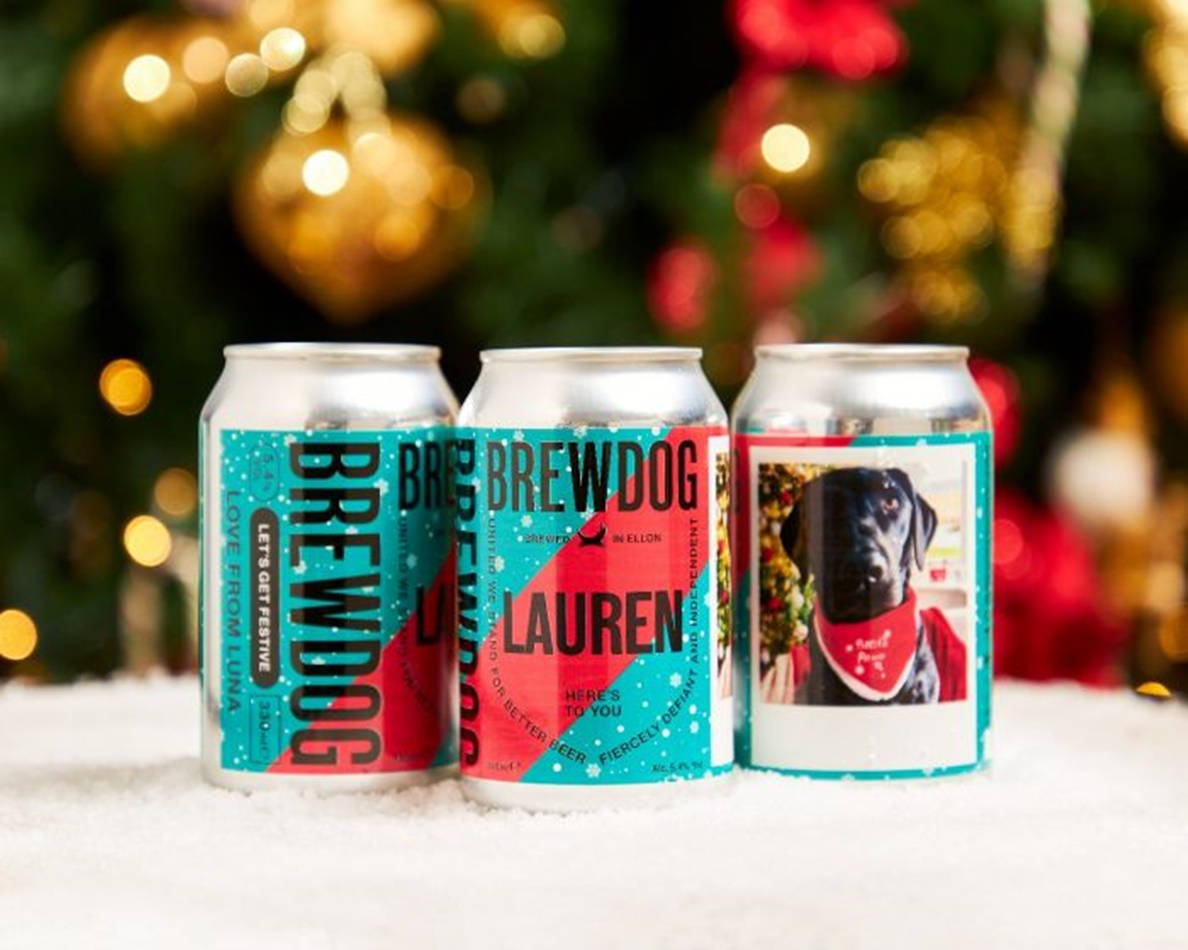 Drink 桌布 壁紙 — 三個個人化的BrewDog啤酒罐，帶有節日設計，放在雪地上，背景是模糊的聖誕樹燈光。