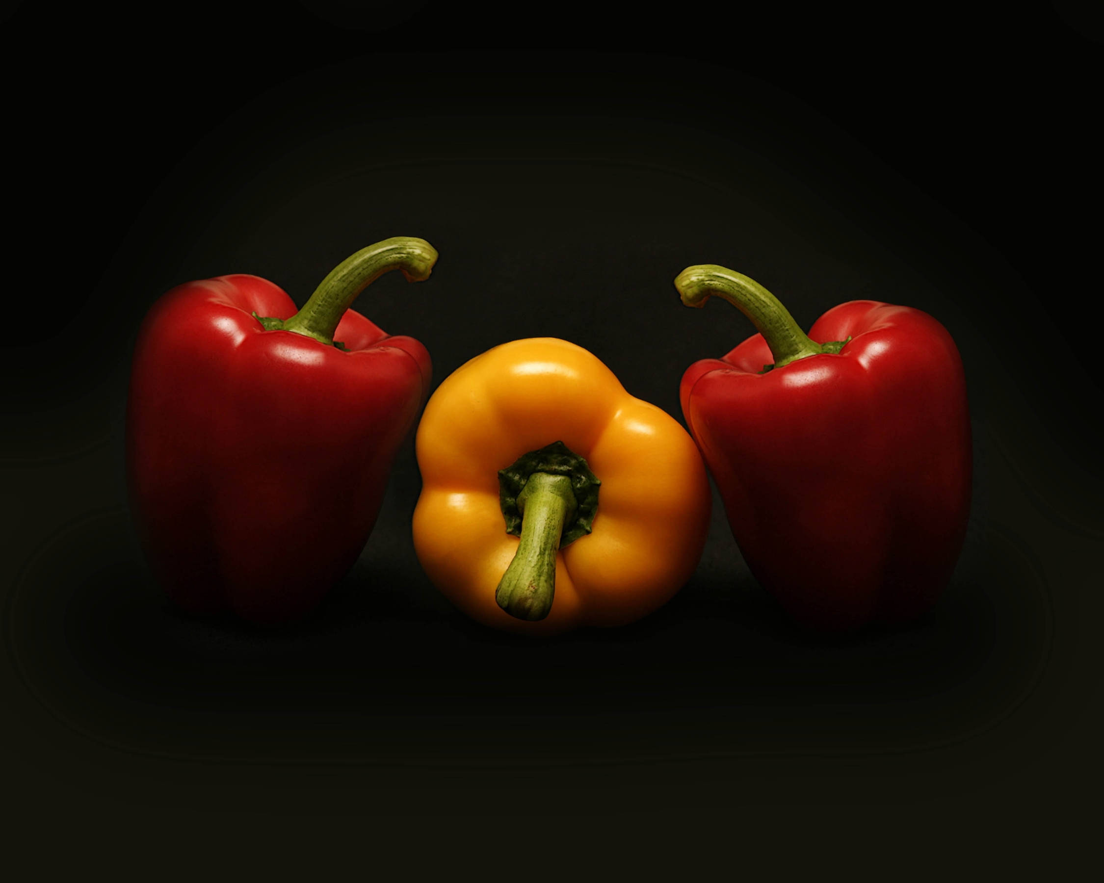 pepper 桌布 壁紙 — 三個光澤的燈籠椒，一個黃色兩旁各有一個紅色，在深黑色背景下鮮明突出。
