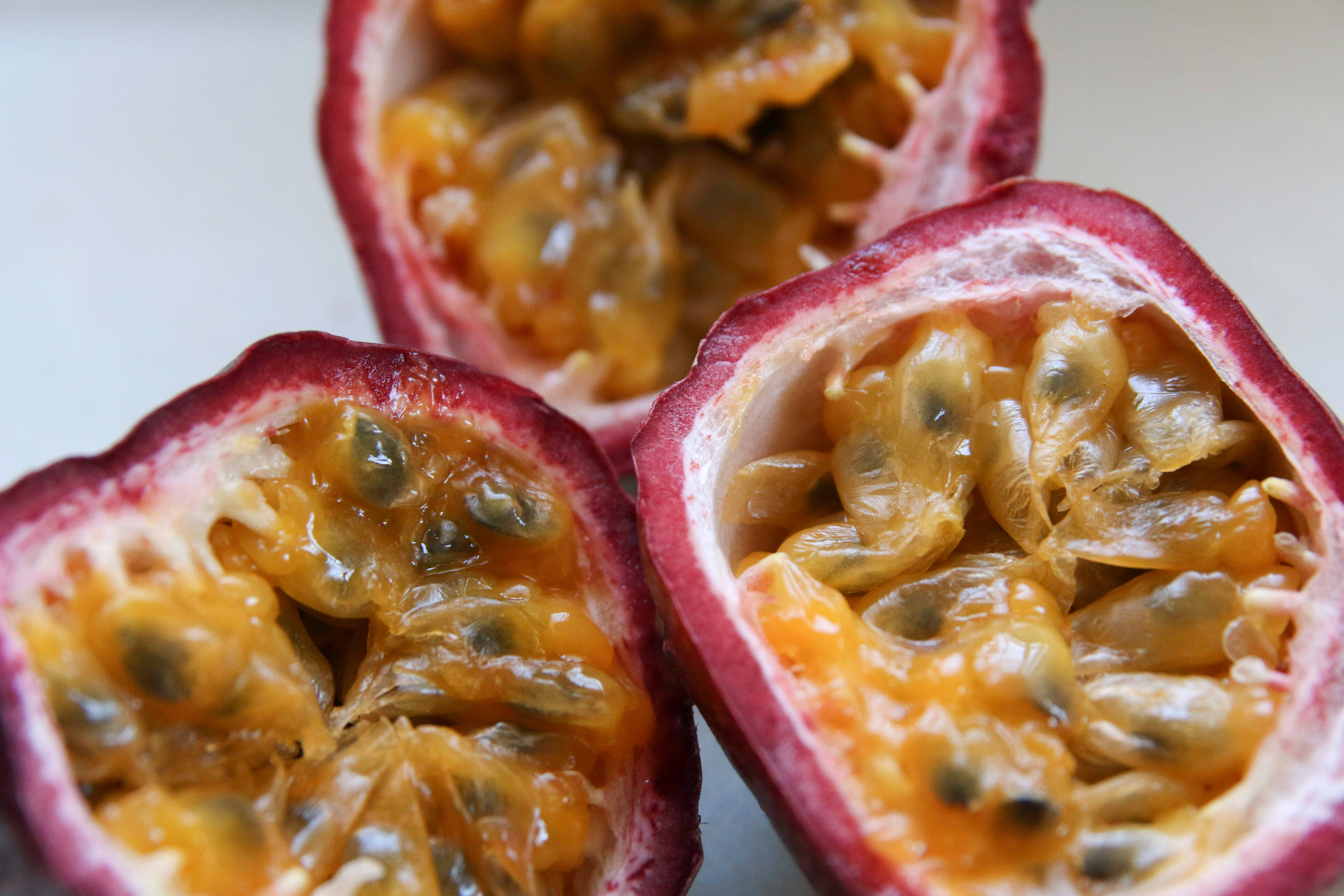 Passion Fruit 桌布 壁紙 — 三個切半的百香果在柔和的白色背景下展現出閃閃發光的金色果肉和深色種子。