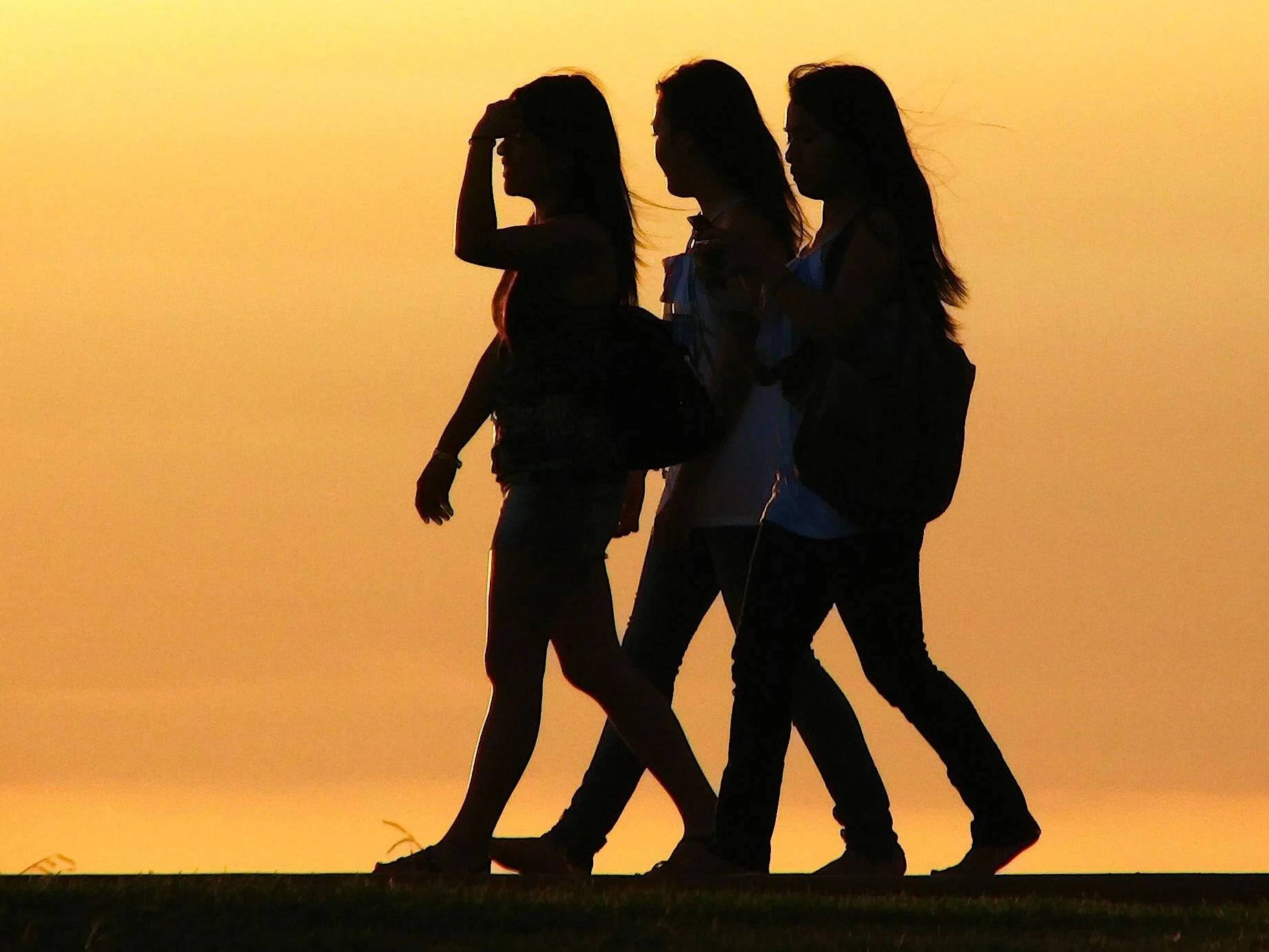 3 Best Friends 桌布 壁紙 — 三個剪影女性在金色日落時並排走過草地。