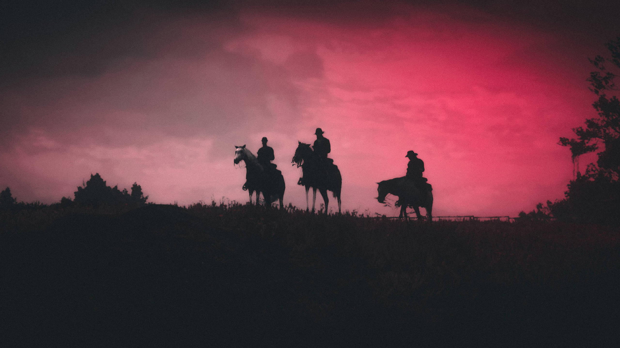 Red Dead Redemtion 2 桌布 壁紙 — 三個剪影騎手騎在馬背上，站在山頂上，背景是戲劇性的粉紅和紫色暮色天空。