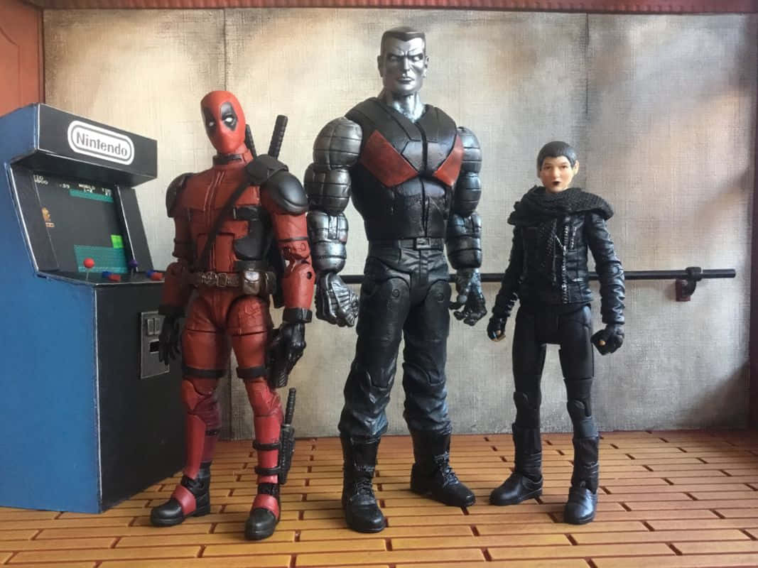 Deadpool And Colossus 桌布 壁紙 — 三個動作人偶 Deadpool、Cable 和一個女性角色站在木地板上的一台復古任天堂街機旁邊。