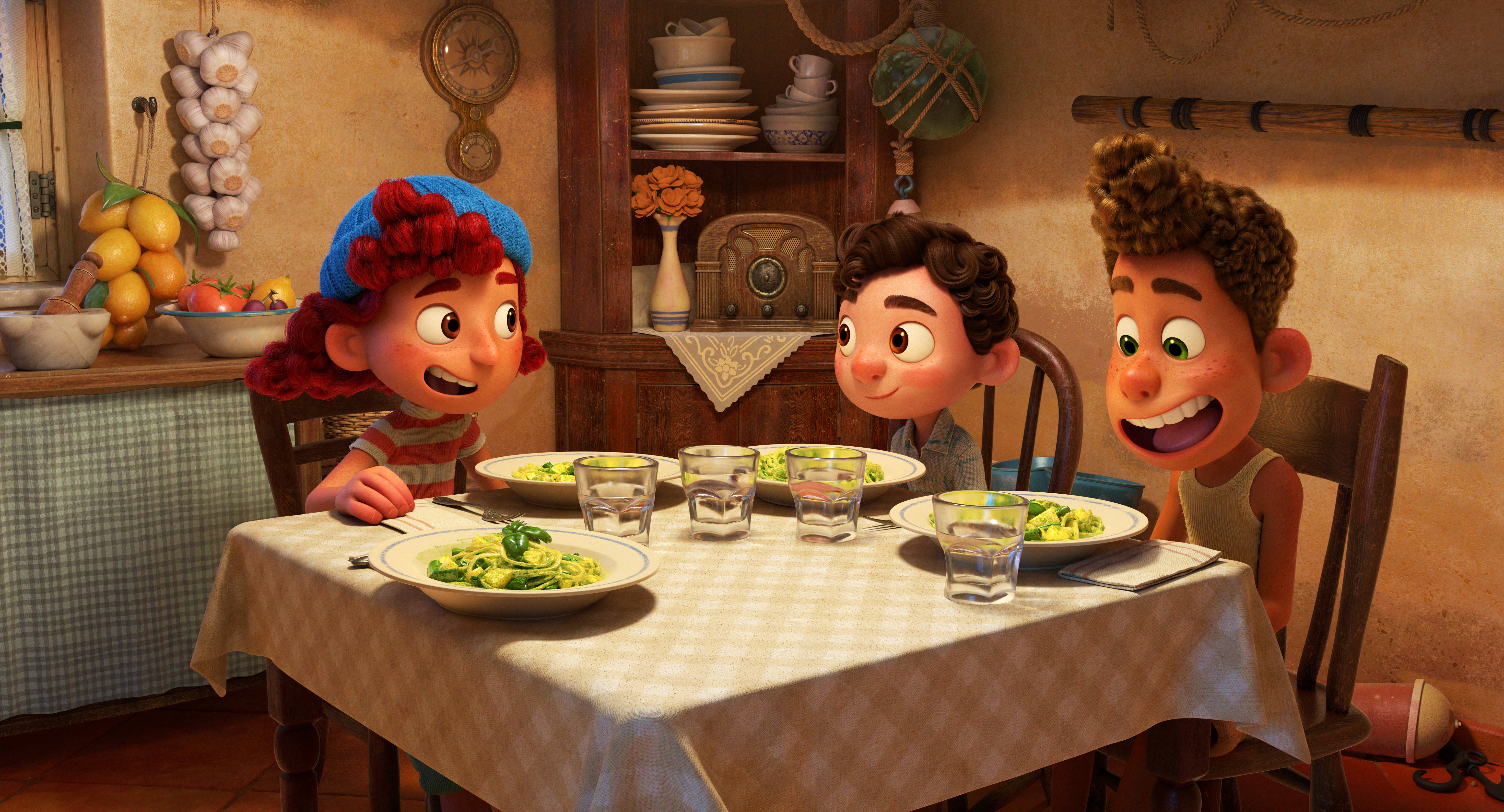 Pixar Luca 桌布 壁紙 — 三個動畫小孩在溫暖照明的鄉村風格廚房裡，圍著鋪滿義大利麵和玻璃杯的格子桌布歡笑。