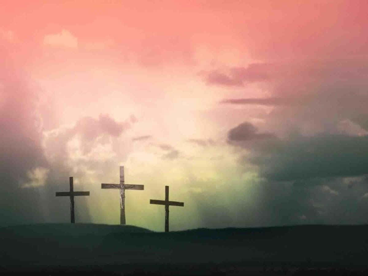 Beautiful Cross 桌布 壁紙 — 三個十字架在黑暗的山丘上，以戲劇性的粉紅色和綠色日落天空為背景，呈現剪影。