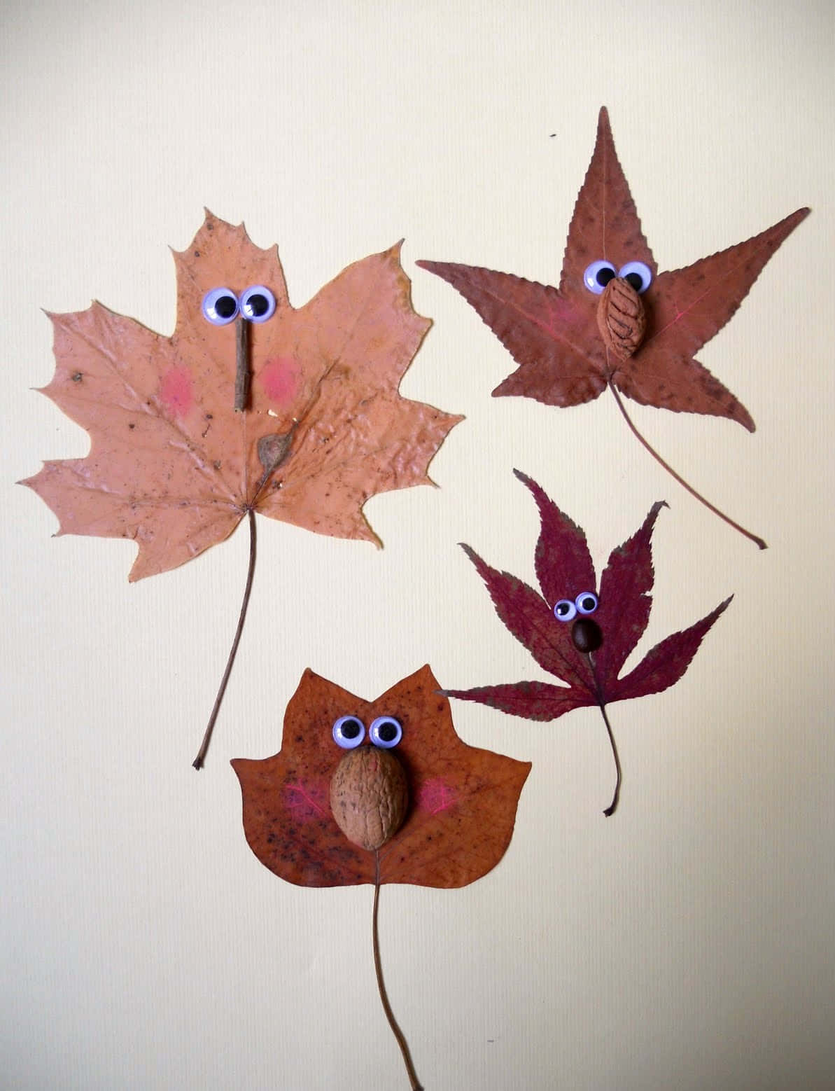Fall Crafts 桌布 壁紙 — 三個古怪的秋季樹葉生物，帶有咕嚕眼和橡子喙，排列在米色背景上。