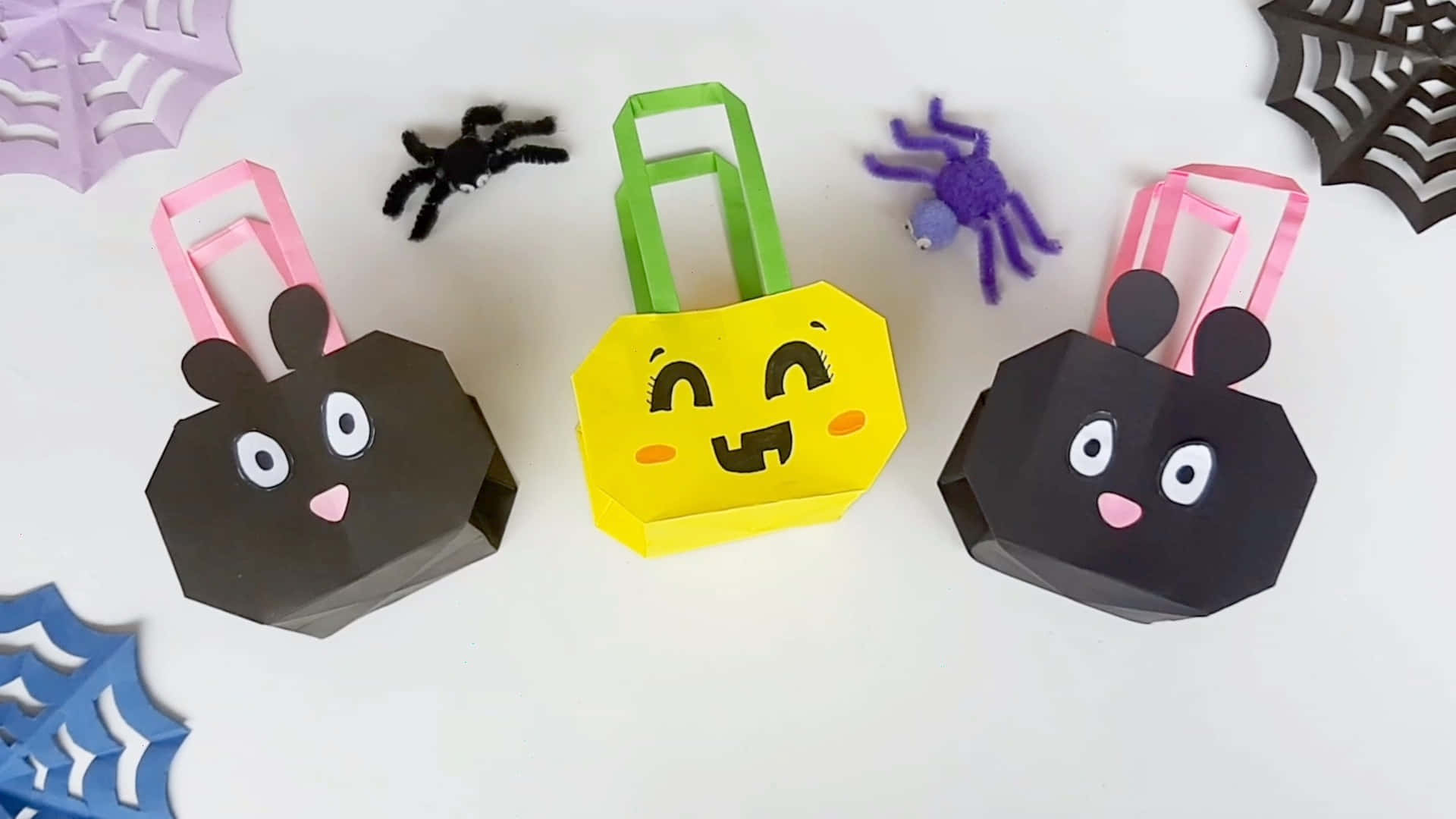 Trick Or Treat Bags 桌布 壁紙 — 三個可愛的紙製萬聖節袋子，形狀像微笑的兔子，帶有蜘蛛裝飾，放在白色表面上。