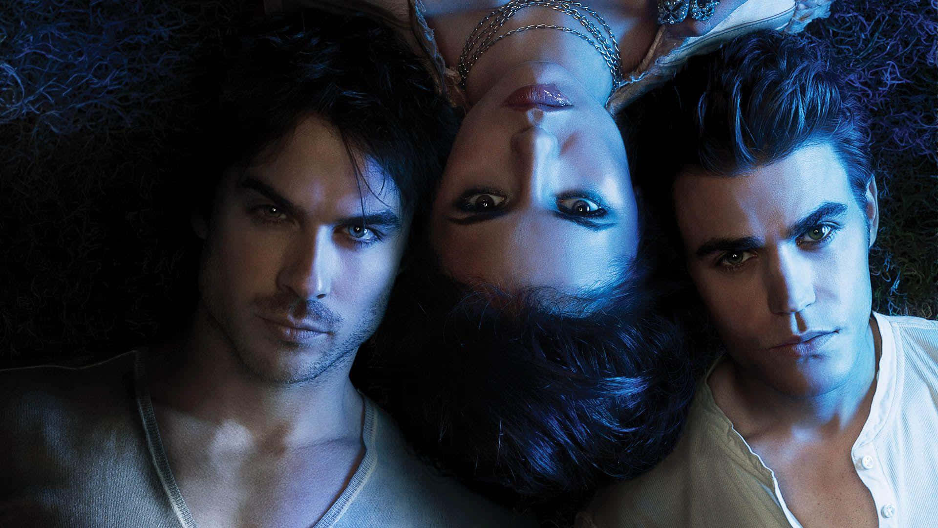 Vampire Diaries Desktop 桌布 壁紙 — 三個吸血鬼在昏暗的藍光中緊靠在一起，眼神強烈，頭髮深色。