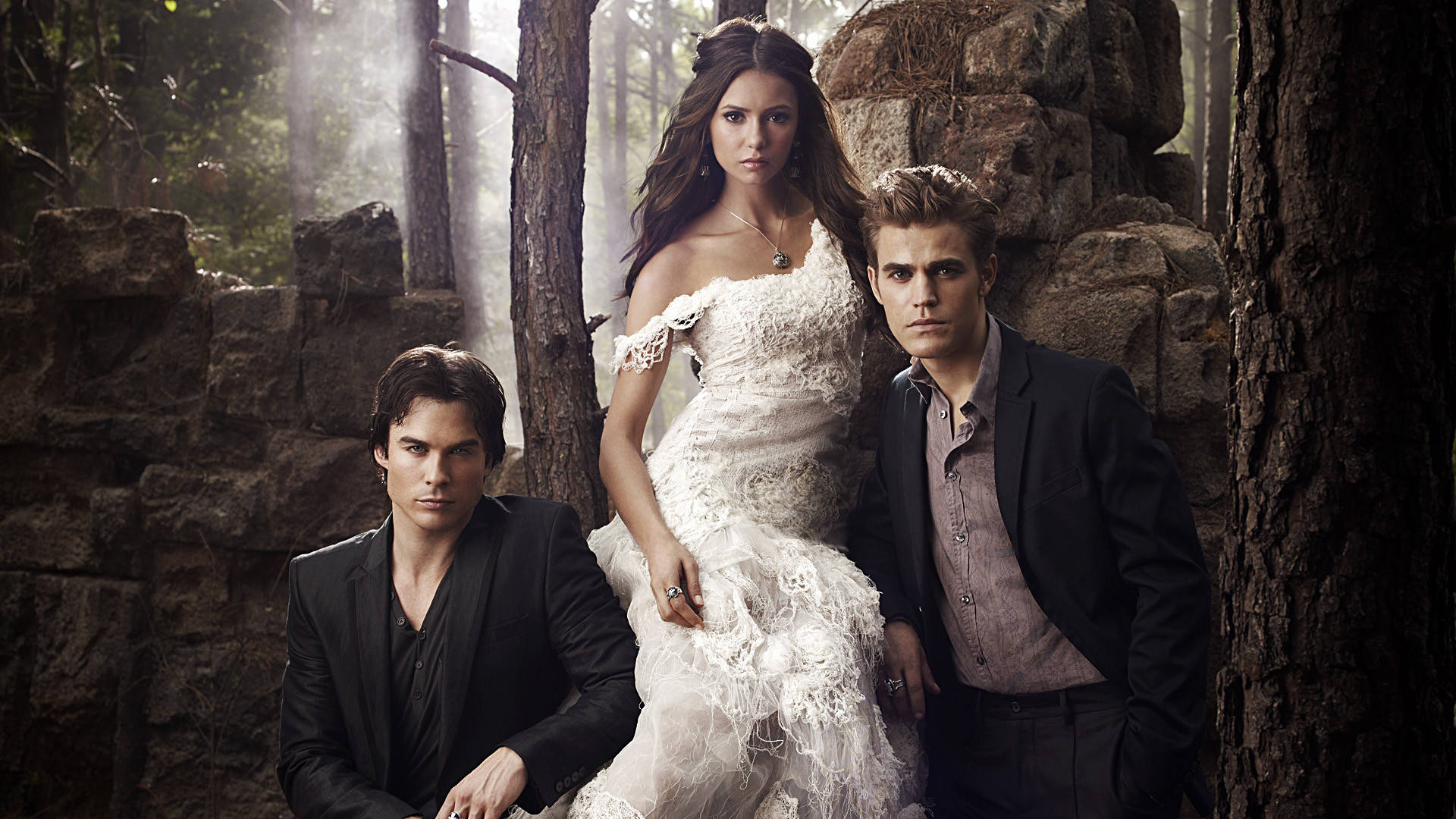Vampire Diaries 桌布 壁紙 — 三個吸血鬼在霧氣瀰漫的森林中，古老的石頭廢墟旁，在柔和的金色光線下戲劇性地擺姿勢。