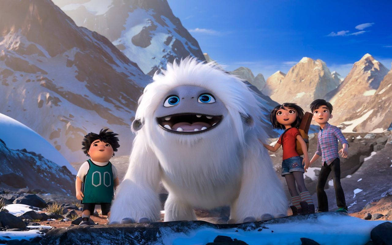 電影動圖 桌布 壁紙 — 三個孩子站在友善的巨型白色雪人旁邊，背景是白雪覆蓋的山景和明亮的藍天。