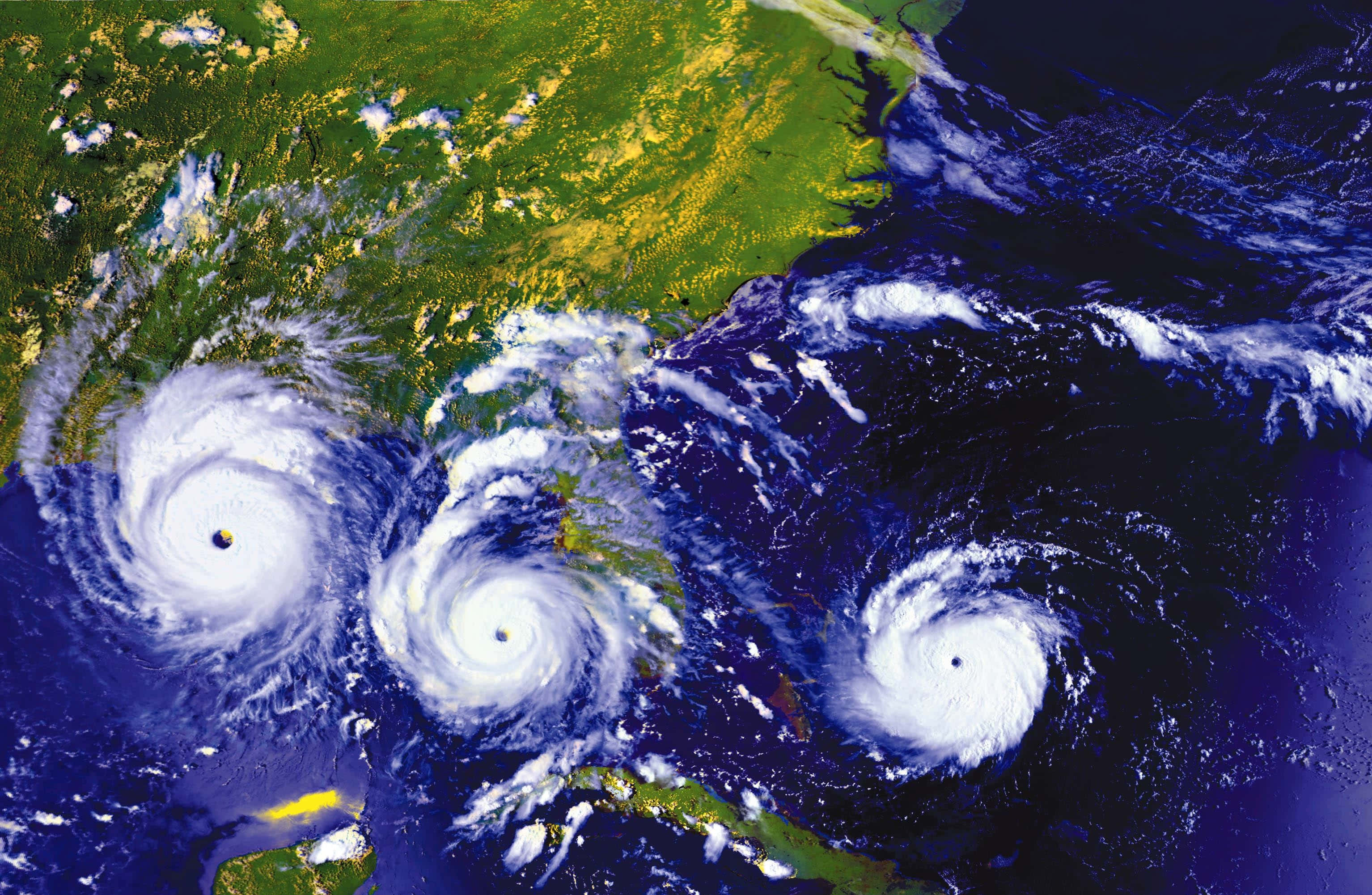 Hurricane 桌布 壁紙 — 三個巨大颶風在大西洋上空旋轉，帶有白色風眼和螺旋雲，背景是綠色陸地和深藍色海洋。