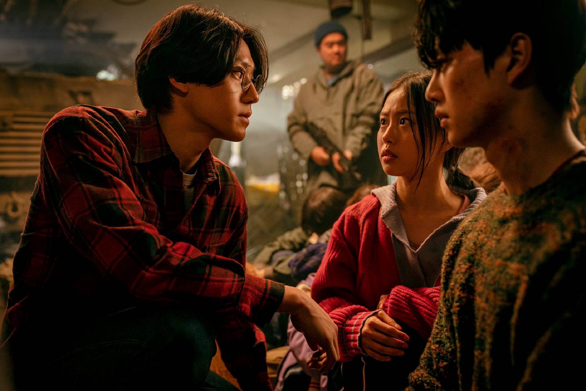 Sweet Home Netflix 桌布 壁紙 — 三個年輕人在燈光昏暗、雜亂的房間裡，在溫暖而戲劇性的燈光下分享一個緊張而專注的時刻。