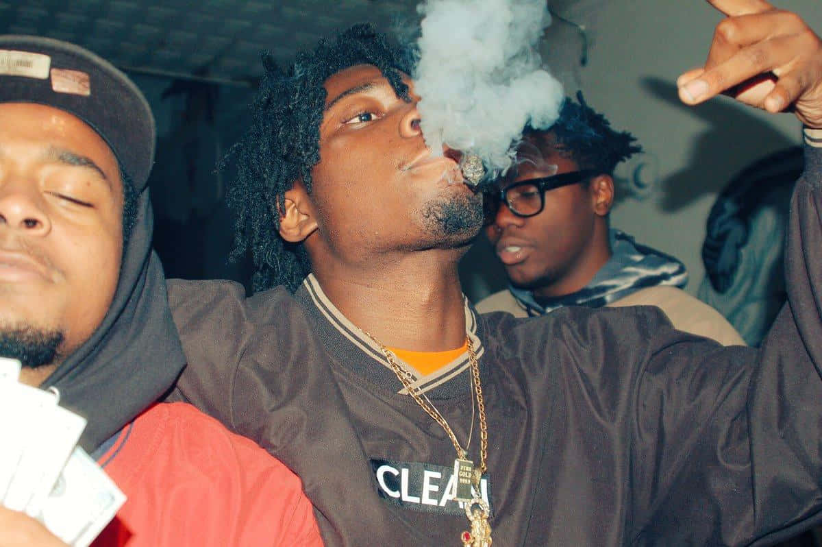 Rappers 桌布 壁紙 — 三個年輕男子在一個燈光昏暗的房間裡，其中一人呼出濃煙，另一人手持現金，第三人戴著眼鏡旁觀。