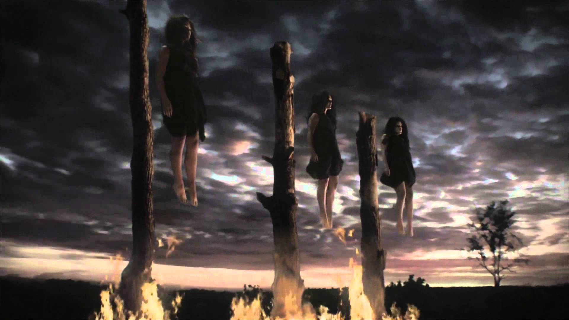 American Horror Story 桌布 壁紙 — 三個幽靈般的女人懸掛在燒焦的樹幹上，背景是暴風雨的黃昏天空，腳下有火焰。