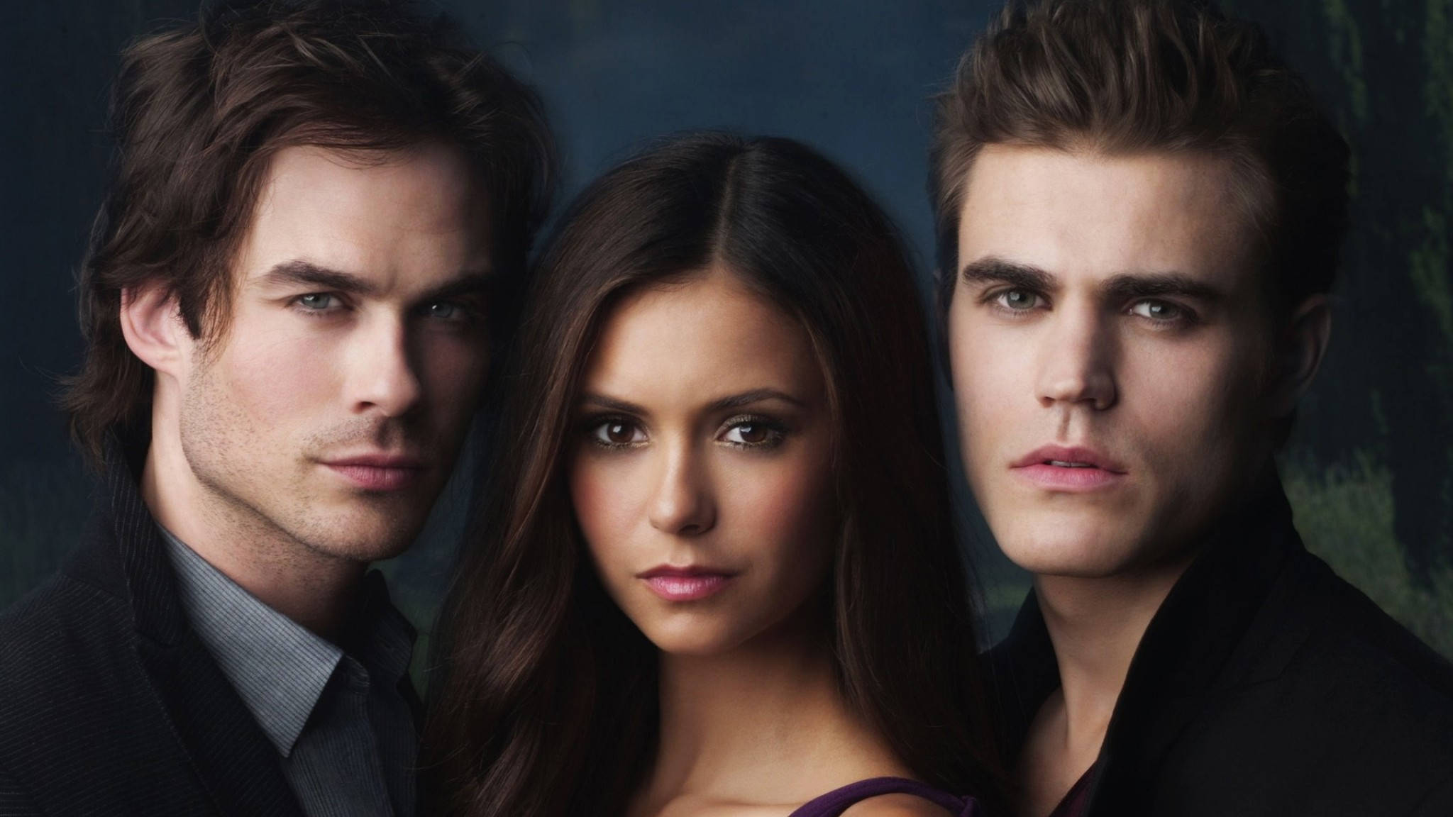 The Vampire Diaries 桌布 壁紙 — 三個強烈的吸血鬼在昏暗陰鬱的背景和柔和燈光下直視觀眾。