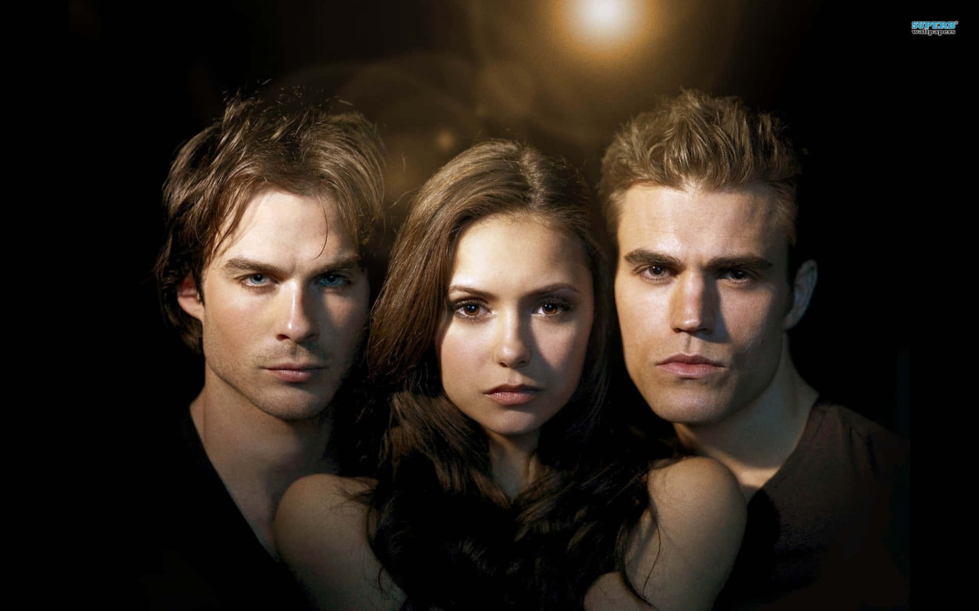The Vampire Diaries iPhone 桌布 壁紙 — 三個強烈的角色在戲劇性的聚光燈下向前凝視，背景為黑暗。
