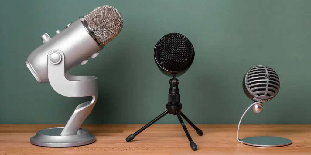 Microphones 桌布 壁紙 — 三個復古和現代麥克風並排放在木桌上，背景是柔和的綠色牆壁。