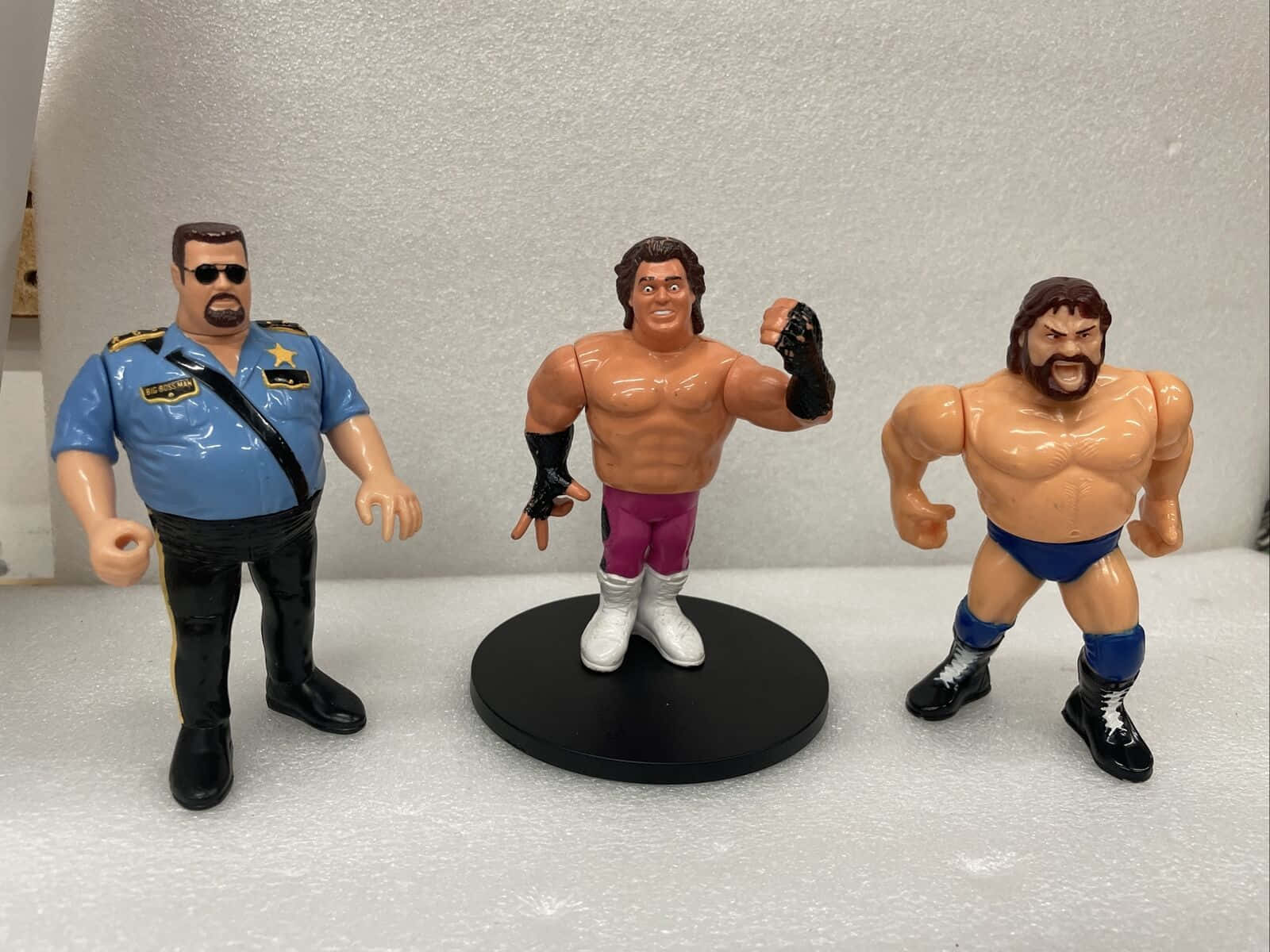 Big Boss Man 桌布 壁紙 — 三個復古摔角動作人偶在泡沫背景上擺姿勢，一個打扮成警長，其他穿著摔角裝備。