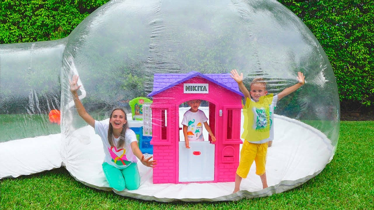 快樂 桌布 壁紙 — 三個快樂的孩子在一個巨大的透明泡泡帳篷內玩耍，帳篷裡有一個粉紅色的遊戲屋，位於茂密的綠色草坪上。
