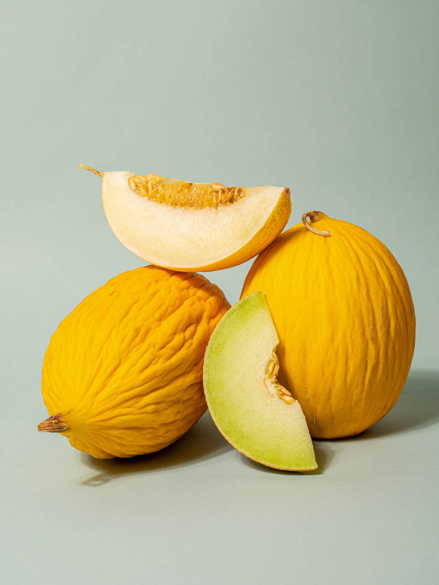 Fruit 桌布 壁紙 — 三個成熟的哈密瓜，帶有紋理的橙色外皮和淡綠色果肉，排列在柔和的灰色背景上。