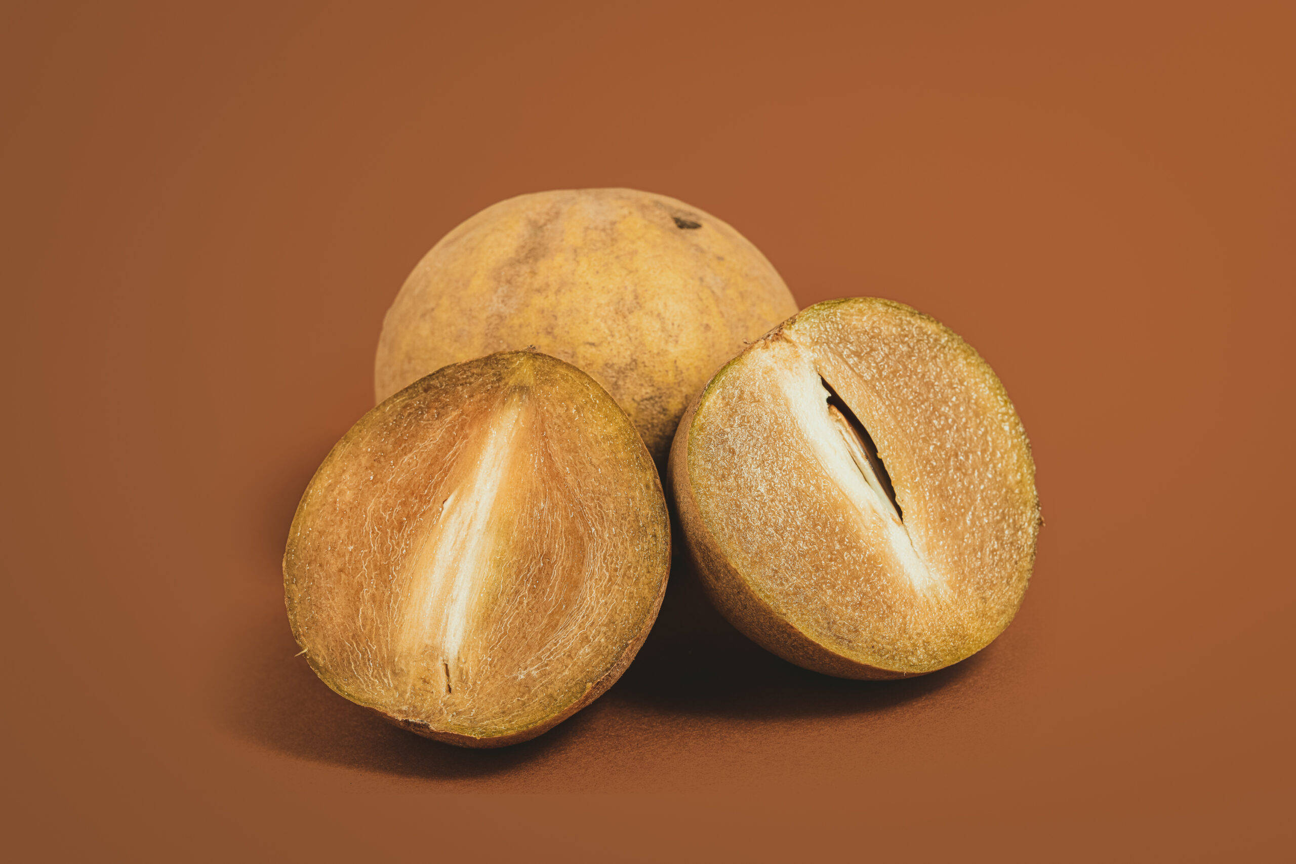 Fruits 桌布 壁紙 — 三個成熟的沙巴果，其中一個切半，露出奶油白色的果肉，背景為溫暖的棕色。